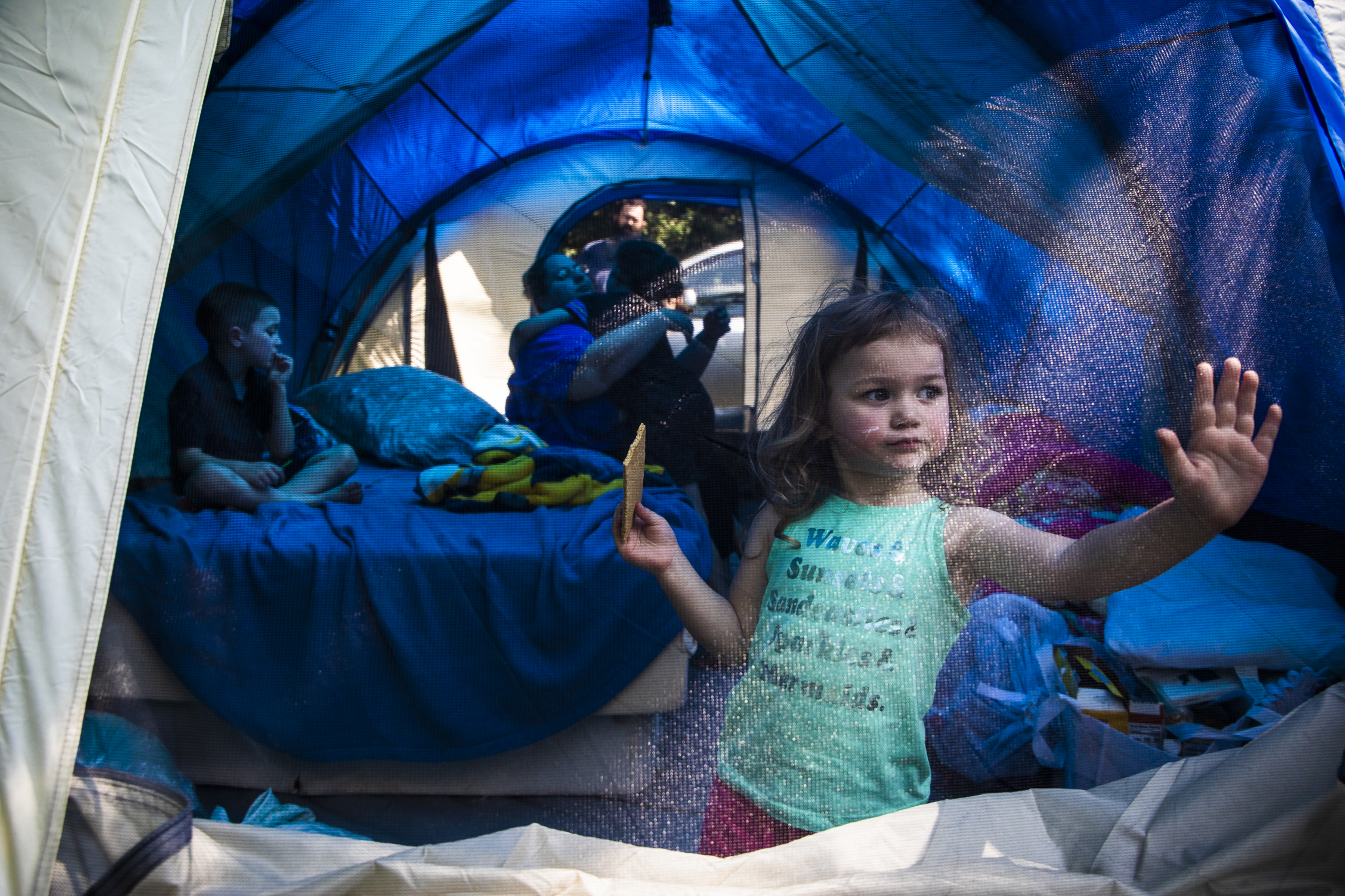 Laya Lupien eats a graham cracker and rests her hand on the door of her family’s tent while trying to escape the summer heat with her brother Dylan (left), mother Mariah, brother Evan, and father Patrick in 2019. The day before, the Lupien family of five was evicted from their home after having their Social Security income taken away, their food stamps reduced, and their rent raised without warning over the span of one year. “Thank you, mommy” said Laya for seemingly no reason. “I really don’t know why you’re thanking me,” said Mariah. “My kids are camping with no roof over their head, and they’re still thankful.”