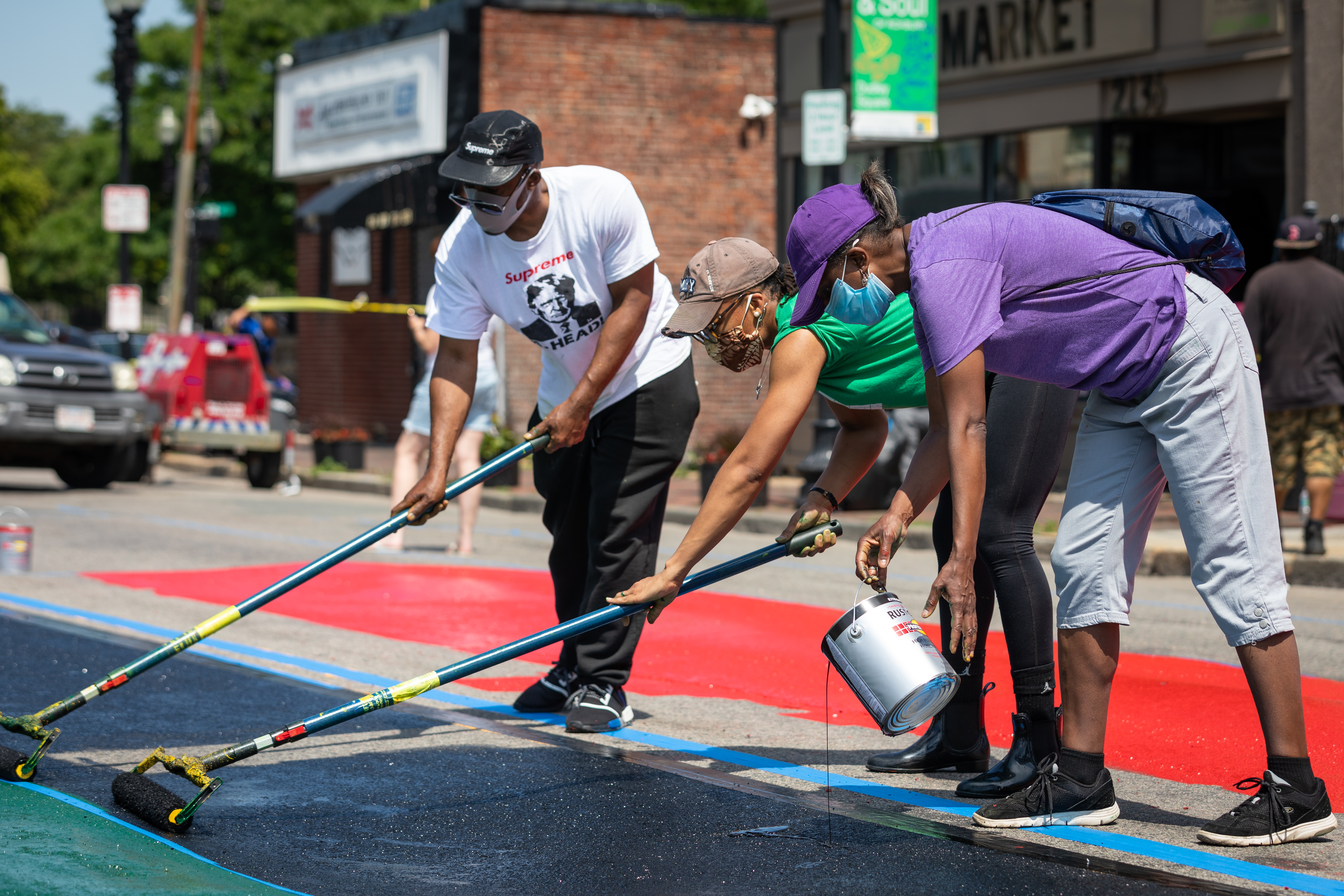 Artists worked on painting the Pan African flag on Washington Street adjacent to the Black Lives Matter sign painted in Nubian Square outside of Black Market in Boston on Sunday.