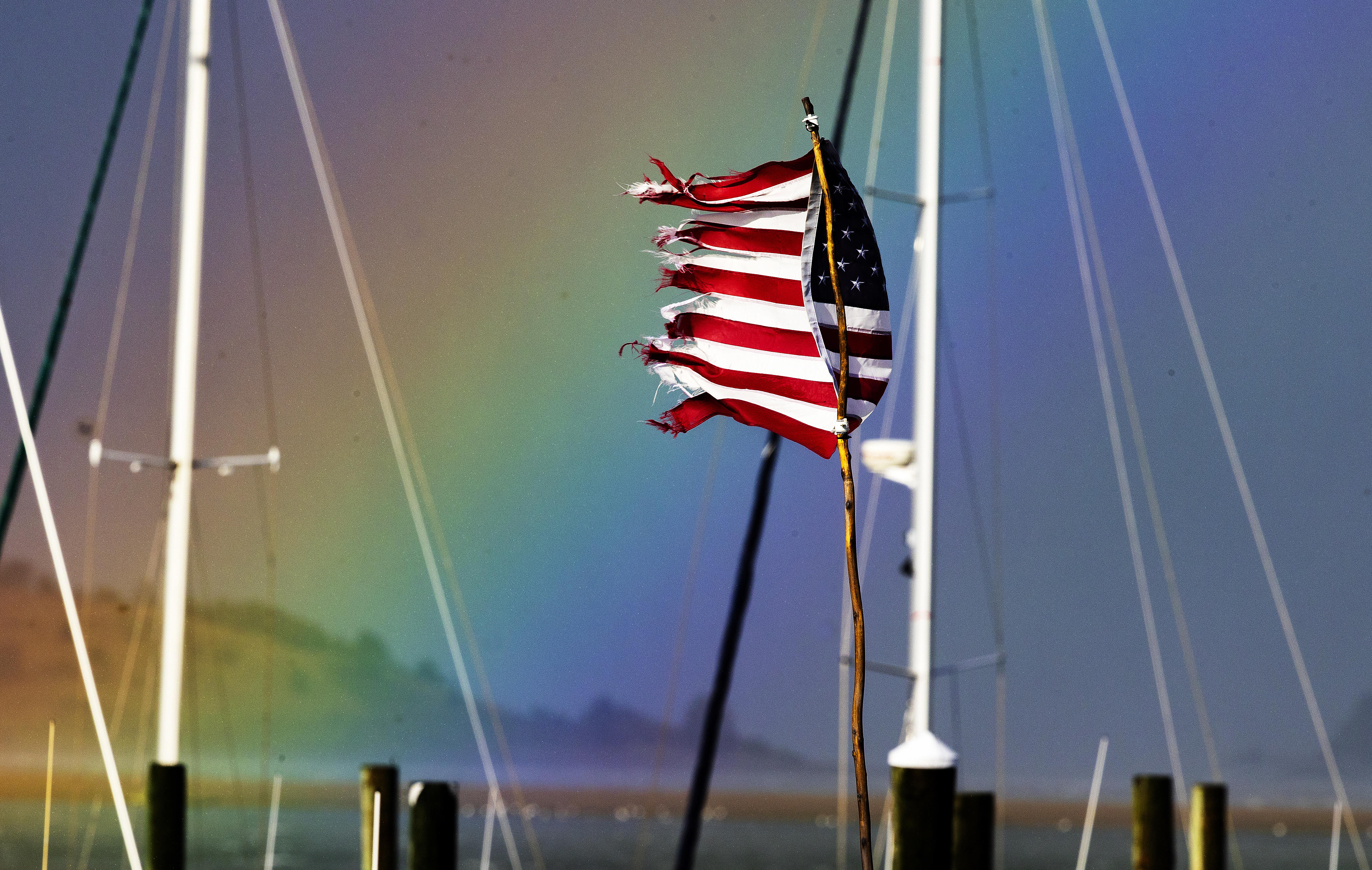 A tattered American flag whipped in the wind at Marina Bay as a rainbow spilled into Boston Harbor near Spectacle Island after an early evening rain storm.