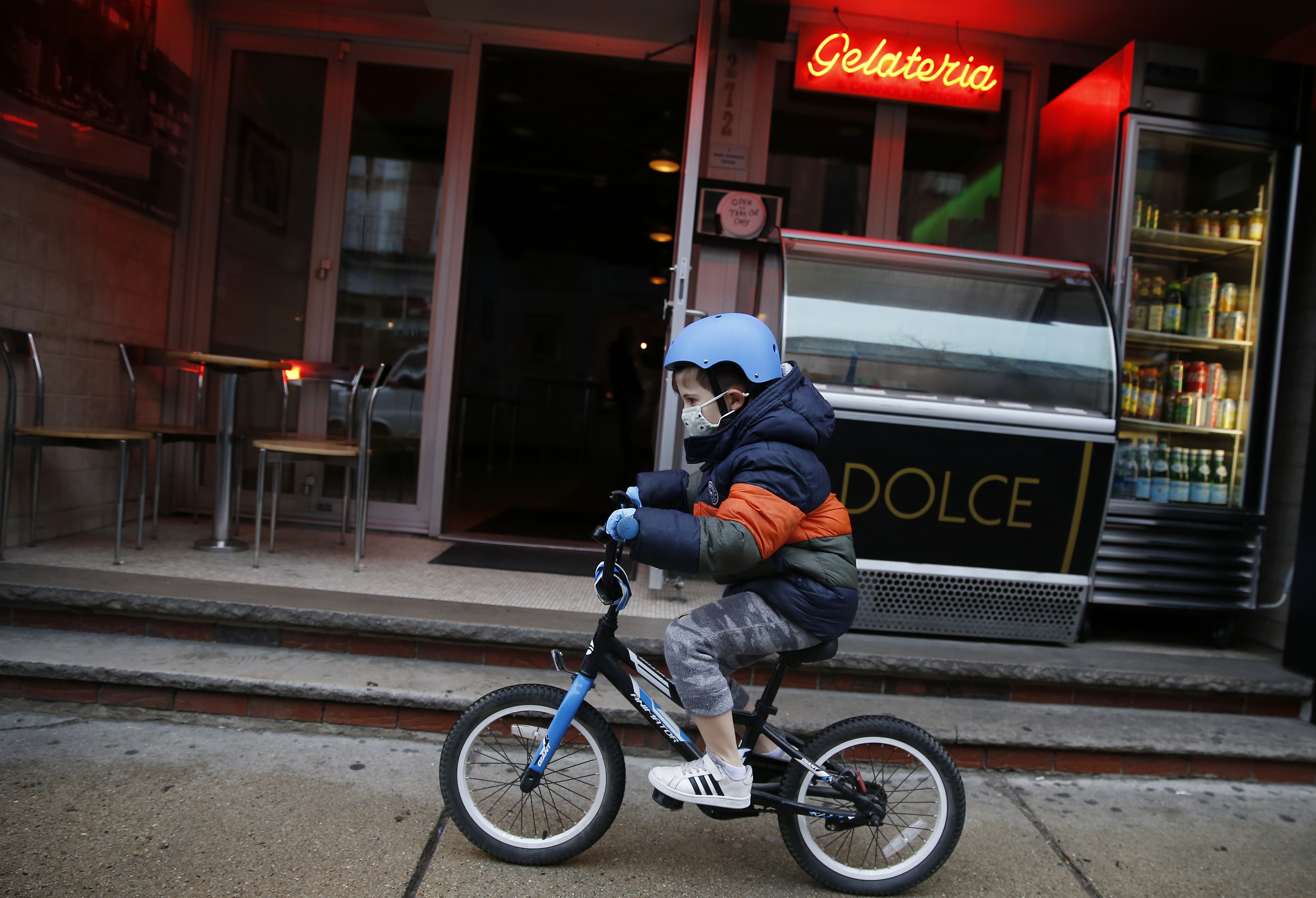 Boston, MA - 3/17/20: Liam Caracciolo, 7, of Boston wears a mask and gloves to protect from coronavirus as he rides his bicycle on the sidewalk along Hanover Street in the North End.  (Jessica Rinaldi/Globe Staff)