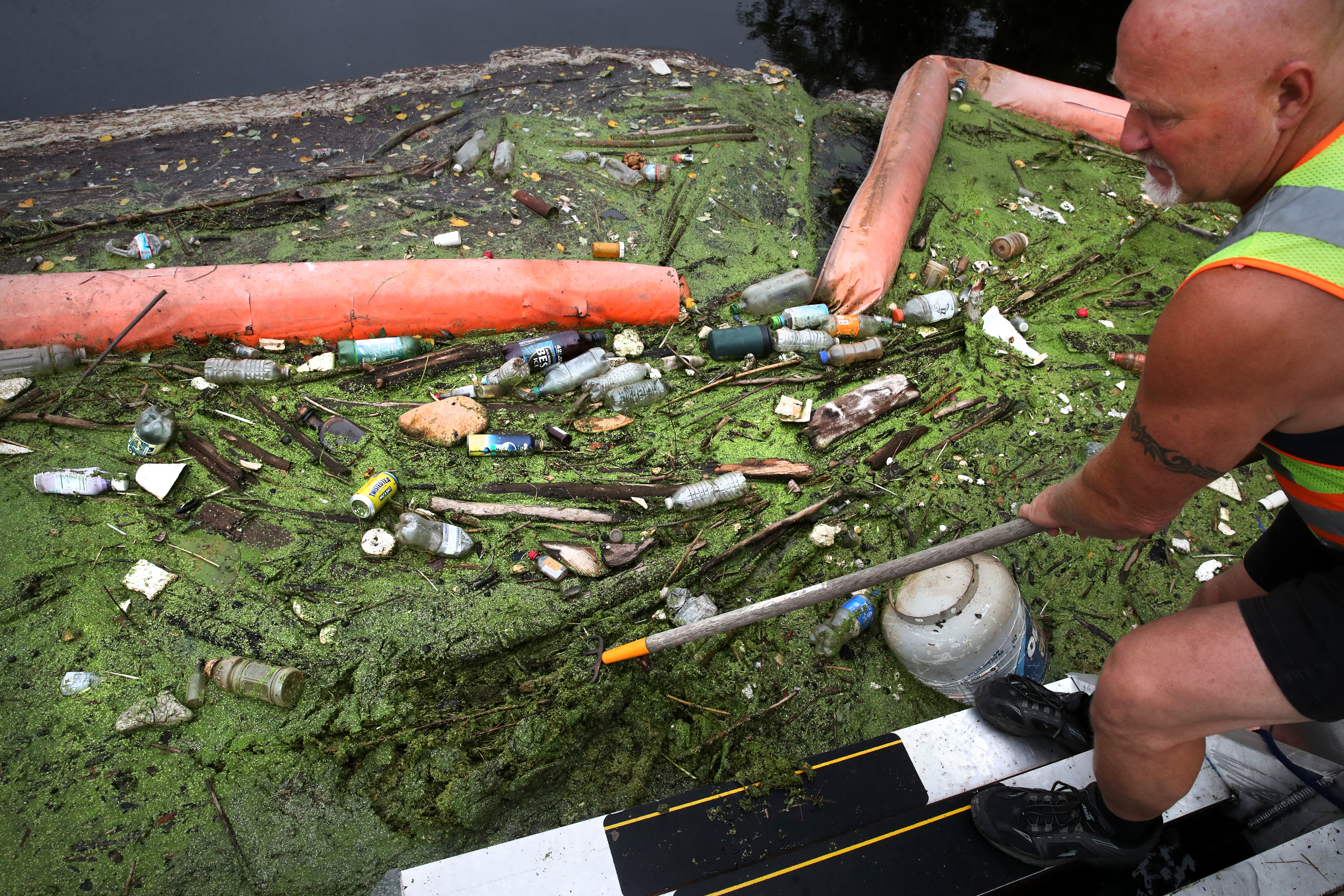 Rocky Morrison, of the Clean River Project, raked through sludge and garbage collected in a boom the Merrimack River in Lawrence.