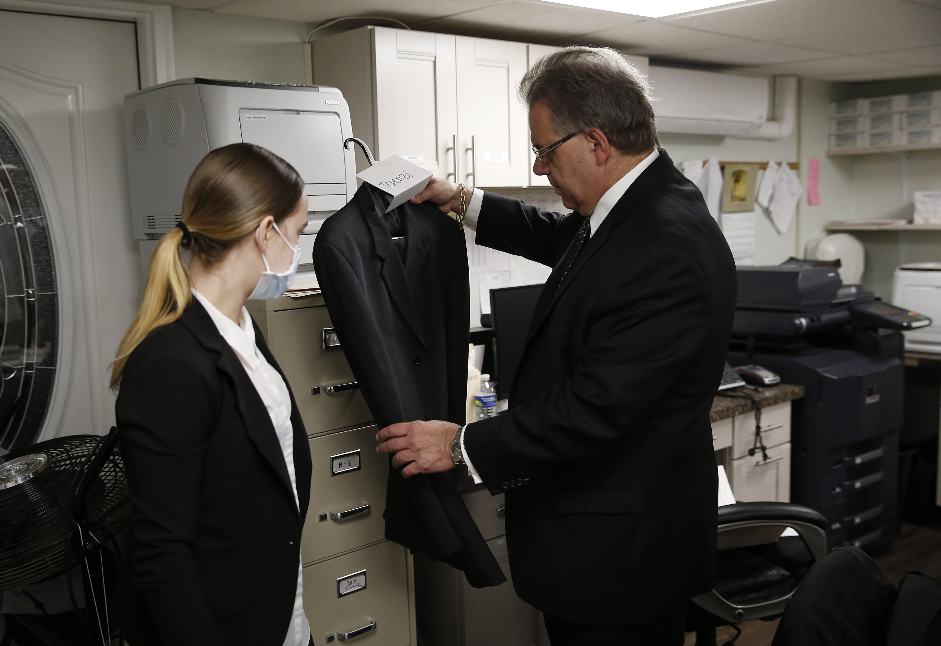 Funeral director Joe Ruggiero Jr. inspected a suit that his daughter, Catie, found hanging in the closet for a client to wear. Because so many people are dying in nursing homes or assisted living facilities, families are not able to get back inside to collect the clothes that they would have dressed their loved ones in for their burial, so Ruggiero has contracted a company to have clothing delivered for burials. In this case, the coat was an old one of his.