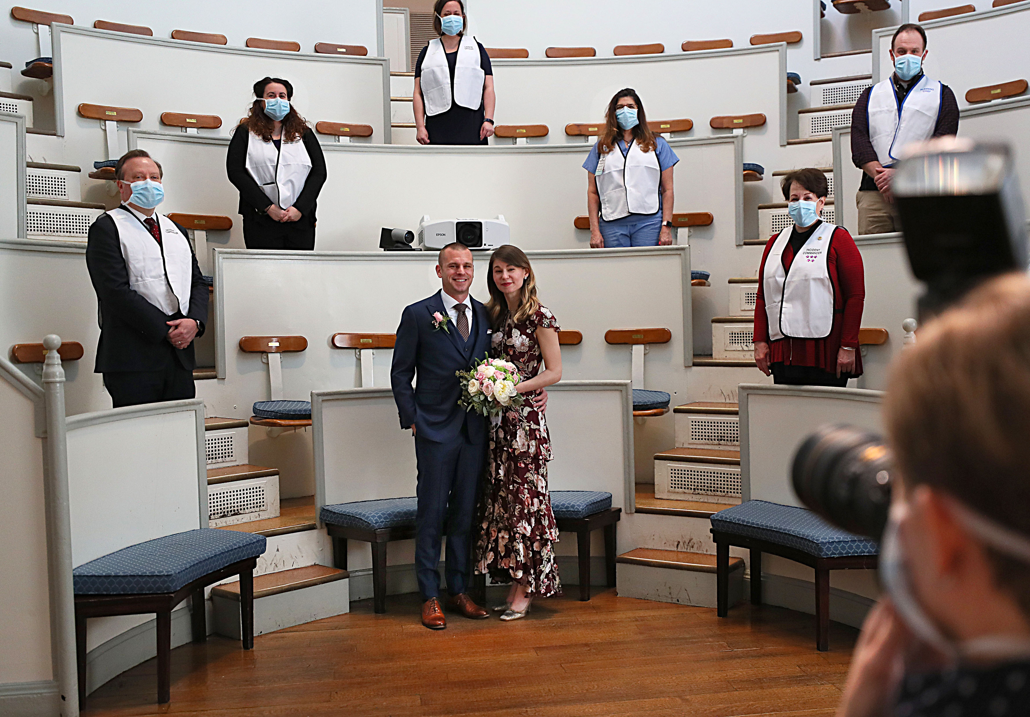 Boston, MA 3/27/2020:  At Massachusetts General Hospital, Jen Andonian, project manager for the MGH Center for Disaster Medicine, and Matt Shearer, senior analyst at the Johns Hopkins Center for Health Security and Research Associate at the Johns Hopkins Bloomberg School of Public Health, got married at the MGH Ether Dome.  They are both epidemiologists   who work in the field of disaster management. Jen and Matt were supposed to get married in Michigan (where Jen is from) March 20 in Ann Arbor, Michigan. Due the coronavirus COVID-19 situation they got married in the famous Ether Dome, where in 1846 the hospital's surgical amphitheater  made history with the first public surgery using anesthetic (Ether.) The MGH General Store and Flower Shop did the flowers.  MGH Nutrition and Food Servic did the cake. MGH Photo Lab took  the photos and  the video to send to their families. (Suzanne Kreiter/Globe Staff)