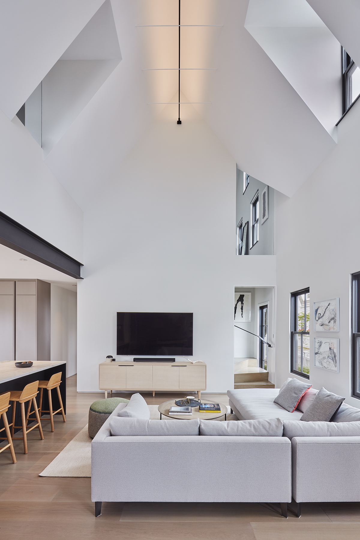 A thin steel strip light runs across the top of the living room, throwing light to the ceiling and adding another black accent. The paintings between the windows are by Taylor O. Thomas.