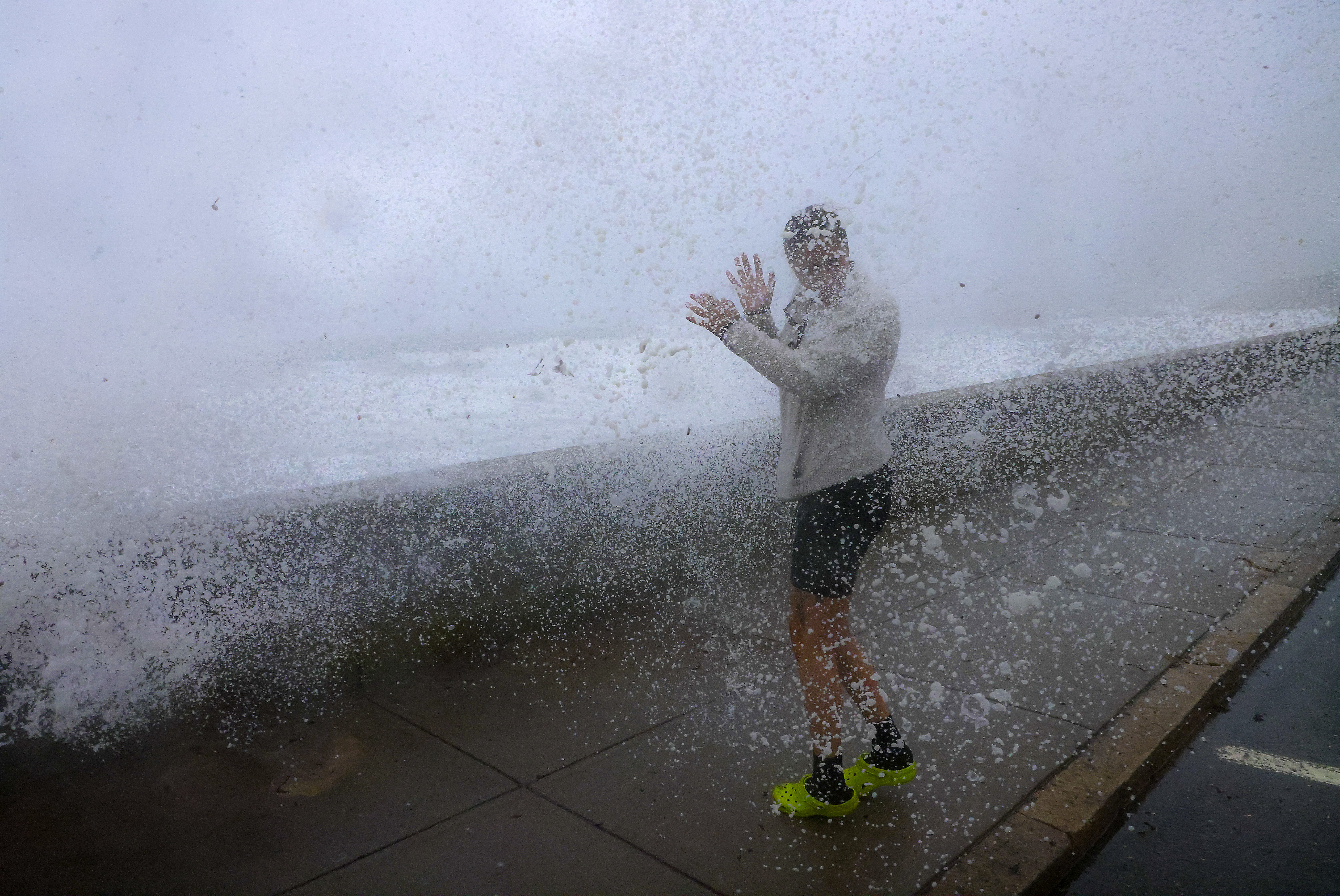 Jasmin Rojo from North Providence and an employee at the Shore House getting doused by foam and sea water, as a wave crests the wall during Tropical Storm Henri.