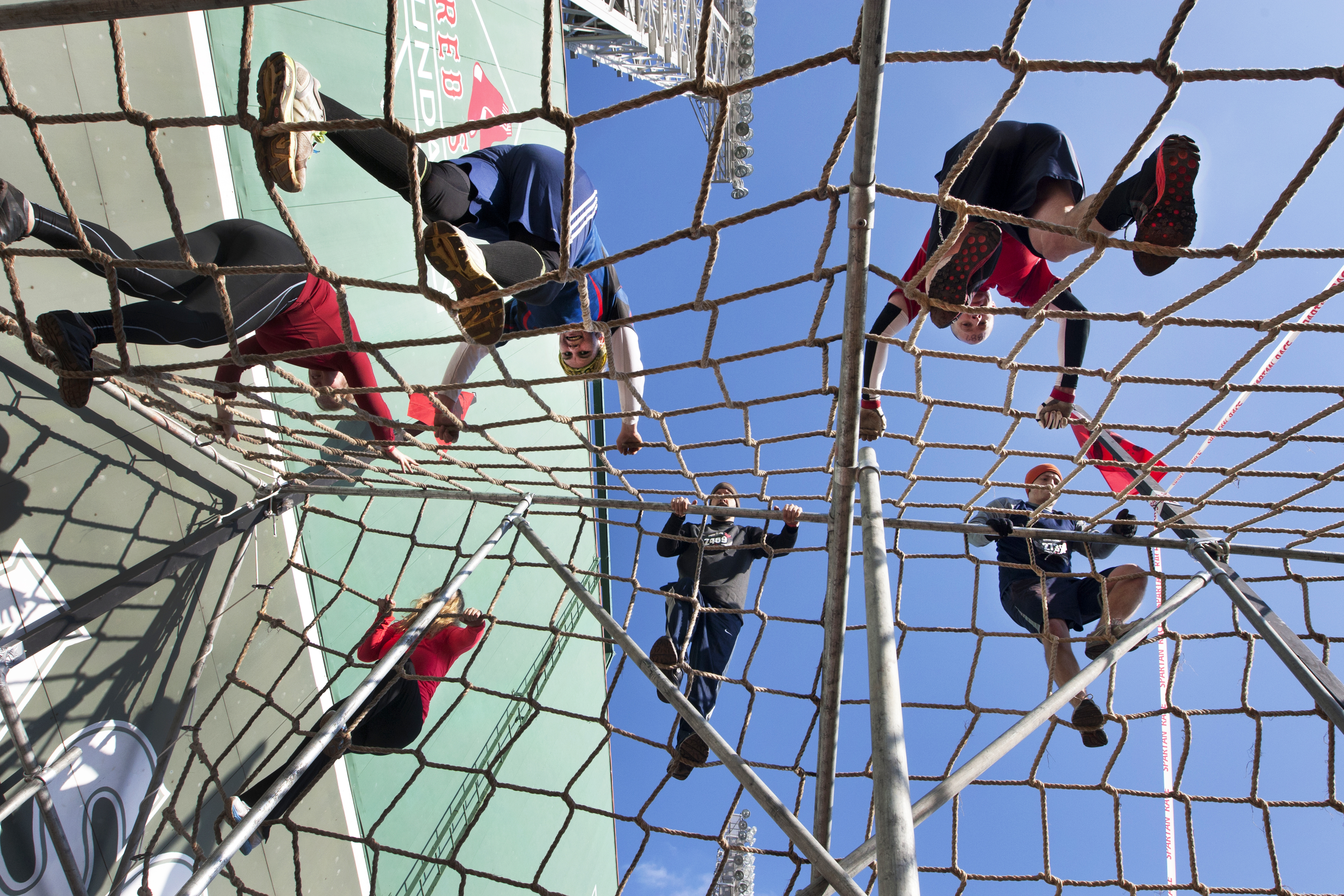 Spartan Race participants scale cargo netting in front of the Green Monster at Fenway Park.