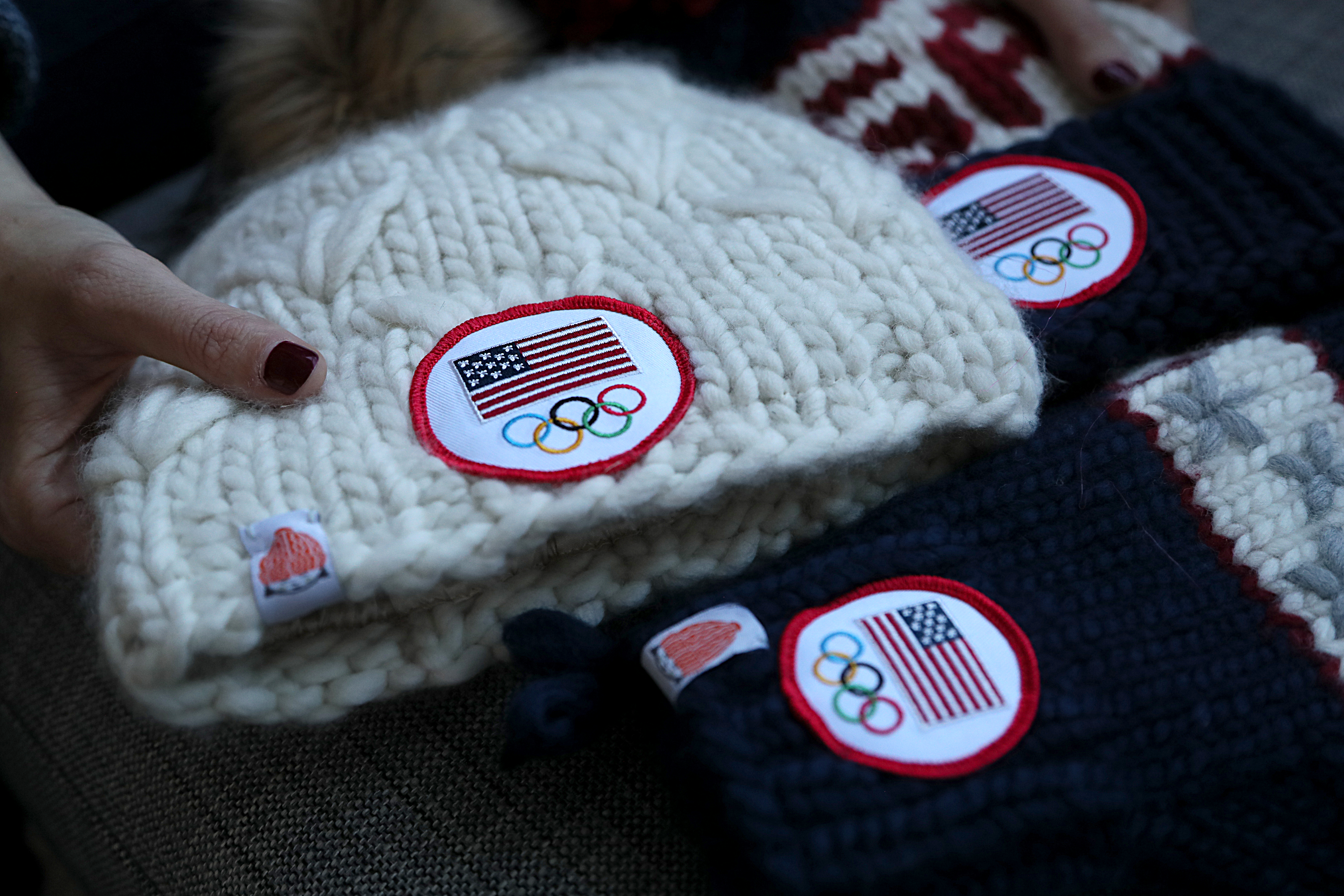 The collection includes red, white, and blue beanies displaying the letters “USA,” along with matching “TEAM” mittens — all with the official Team USA mark sewn in.