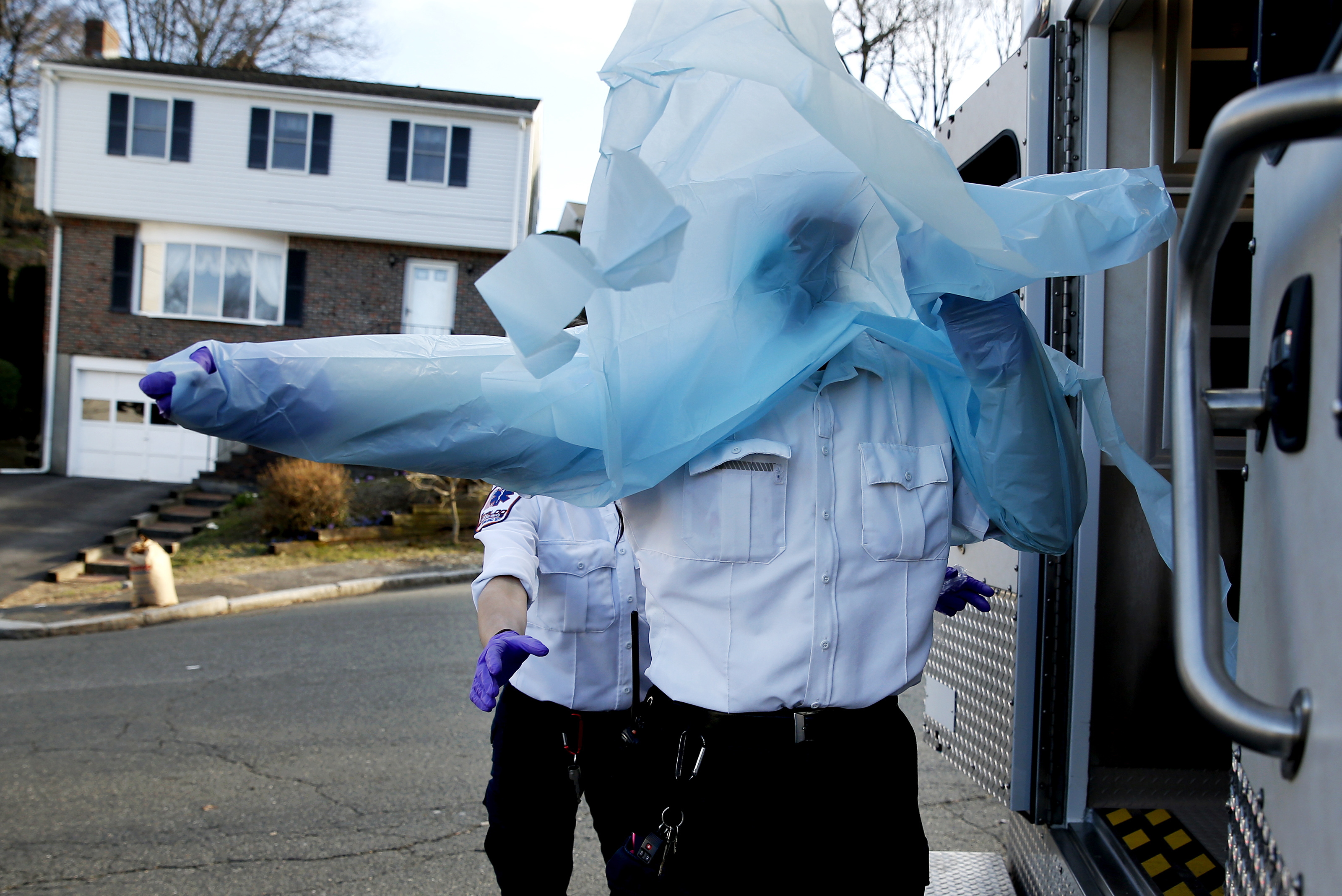 Monday, 5:38 p.m. A gust of wind caught the plastic gown that Ricky used for protection as Emily reached out to fasten the ties so that he can get in the back of the ambulance with a patient. A woman in the patient’s home had shouted out to tell them that he did not have coronavirus, but they presume that anyone they help might be positive for COVID-19.