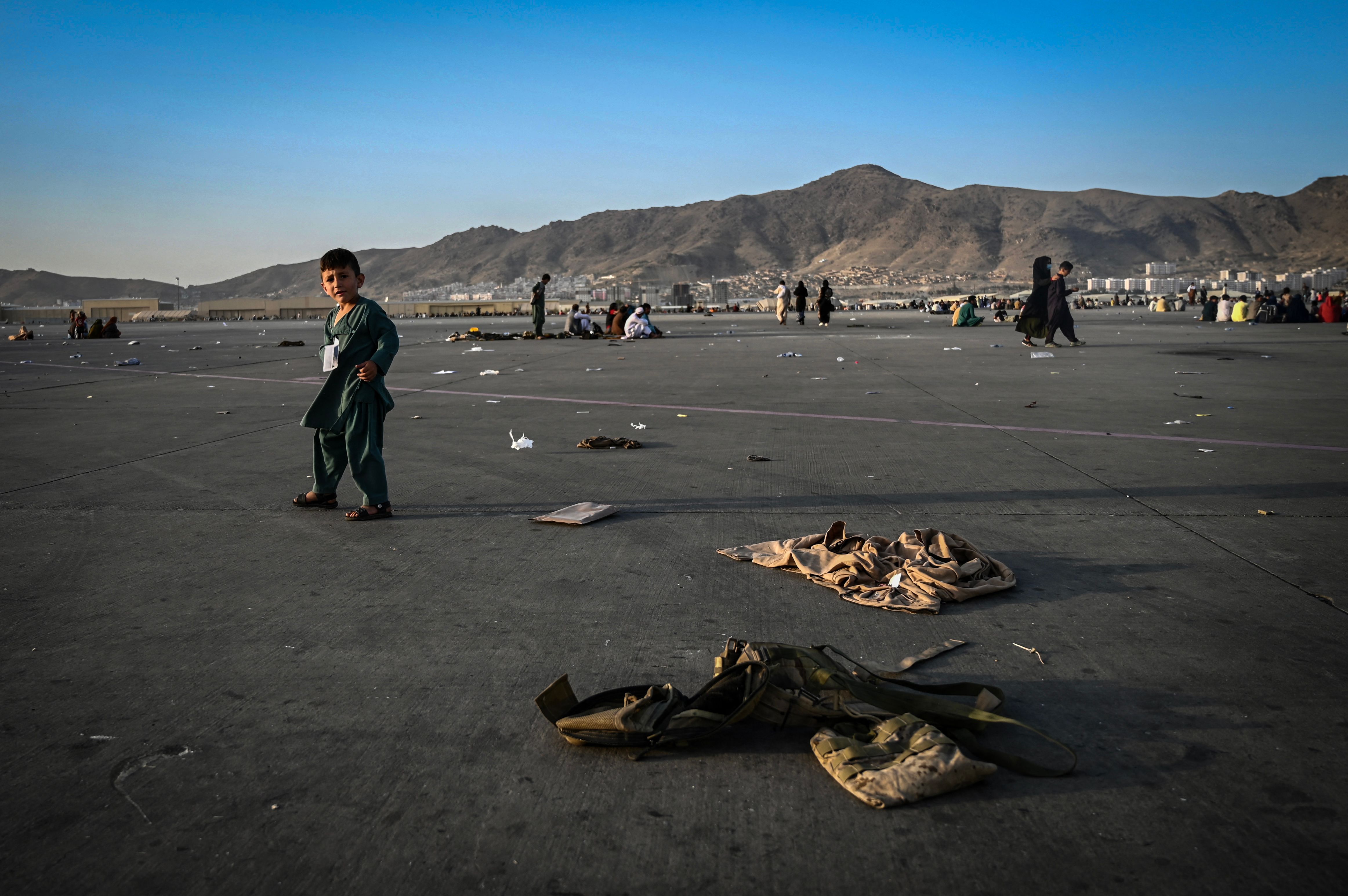 An Afghan child walked near military uniforms as he waited with elders at the Kabul airport.