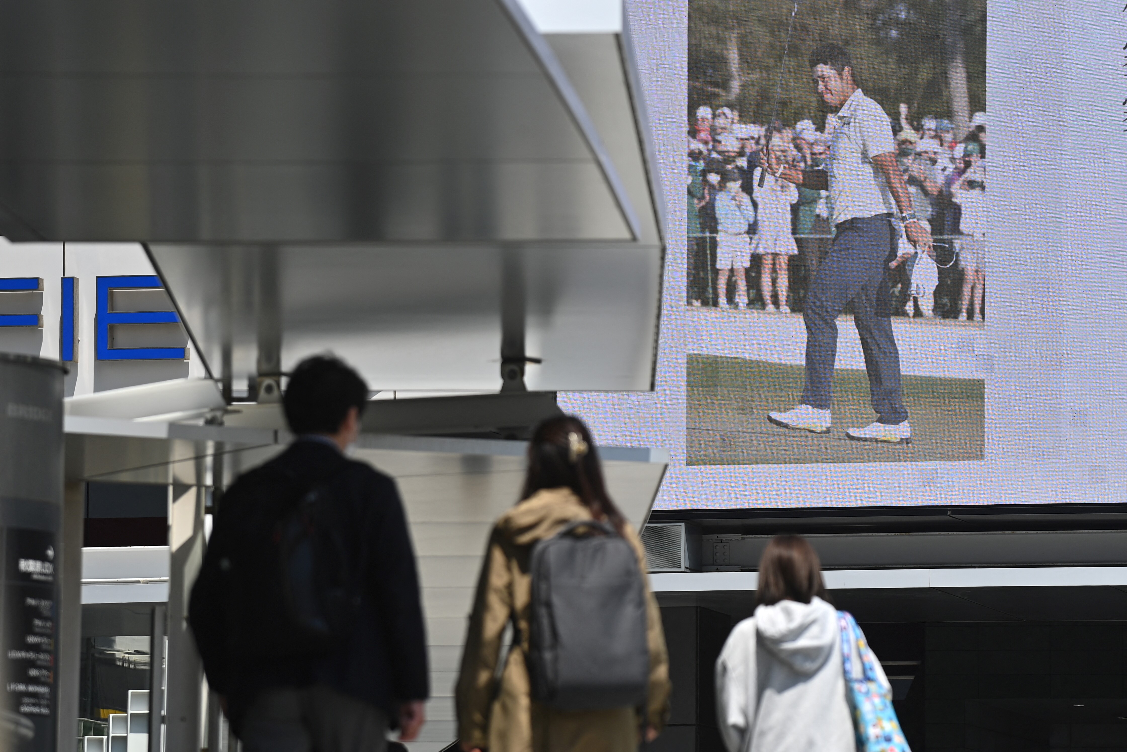 People in the Akihabara district of Tokyo walk in front of a screen showing the news of Japan's Hideki Matsuyama winning the 85th Masters.