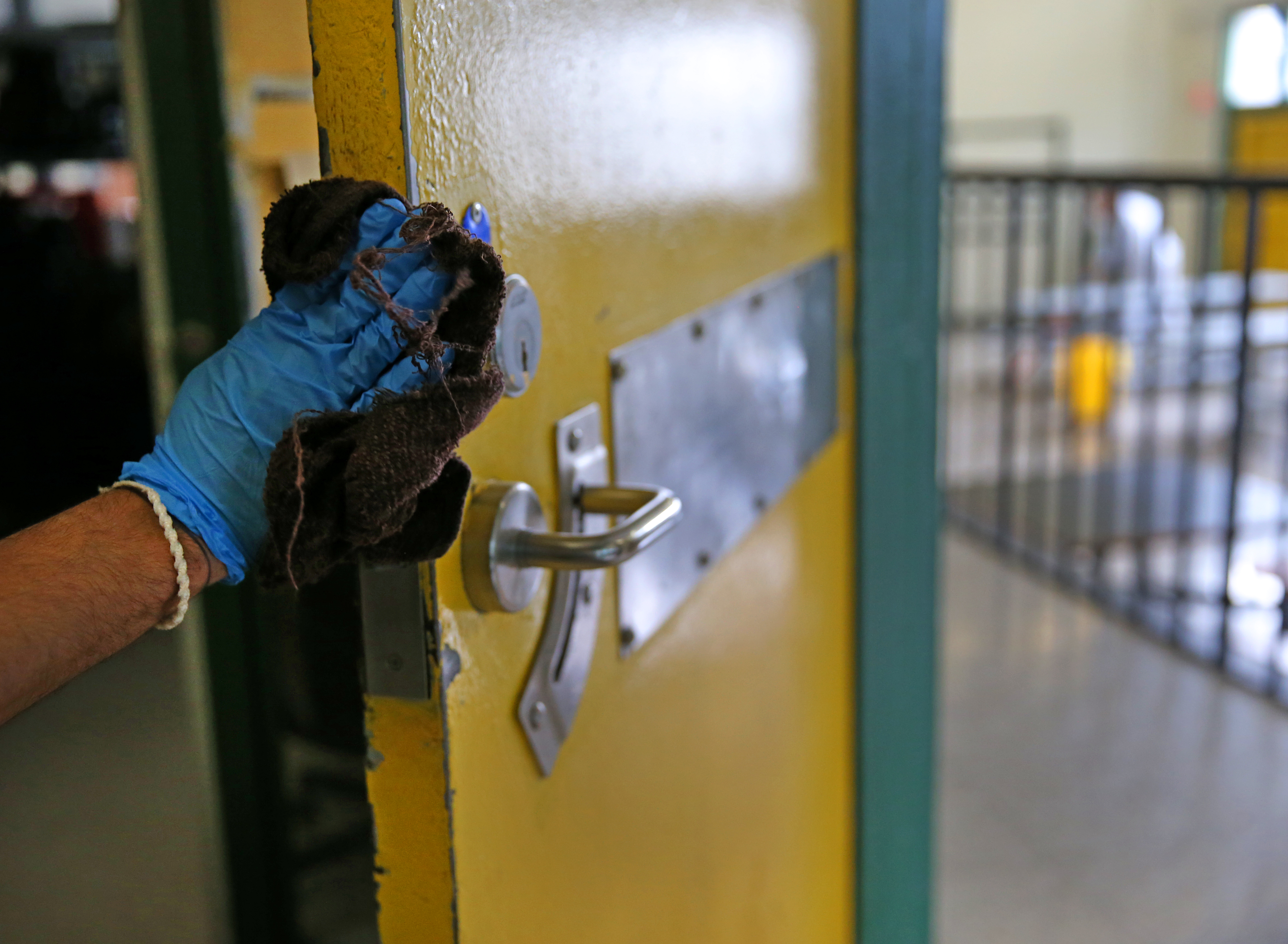 An inmate wearing protective gloves wiped down a general population room door after it was sanitized at the Worcester County House Of Corrections in West Boylston.
