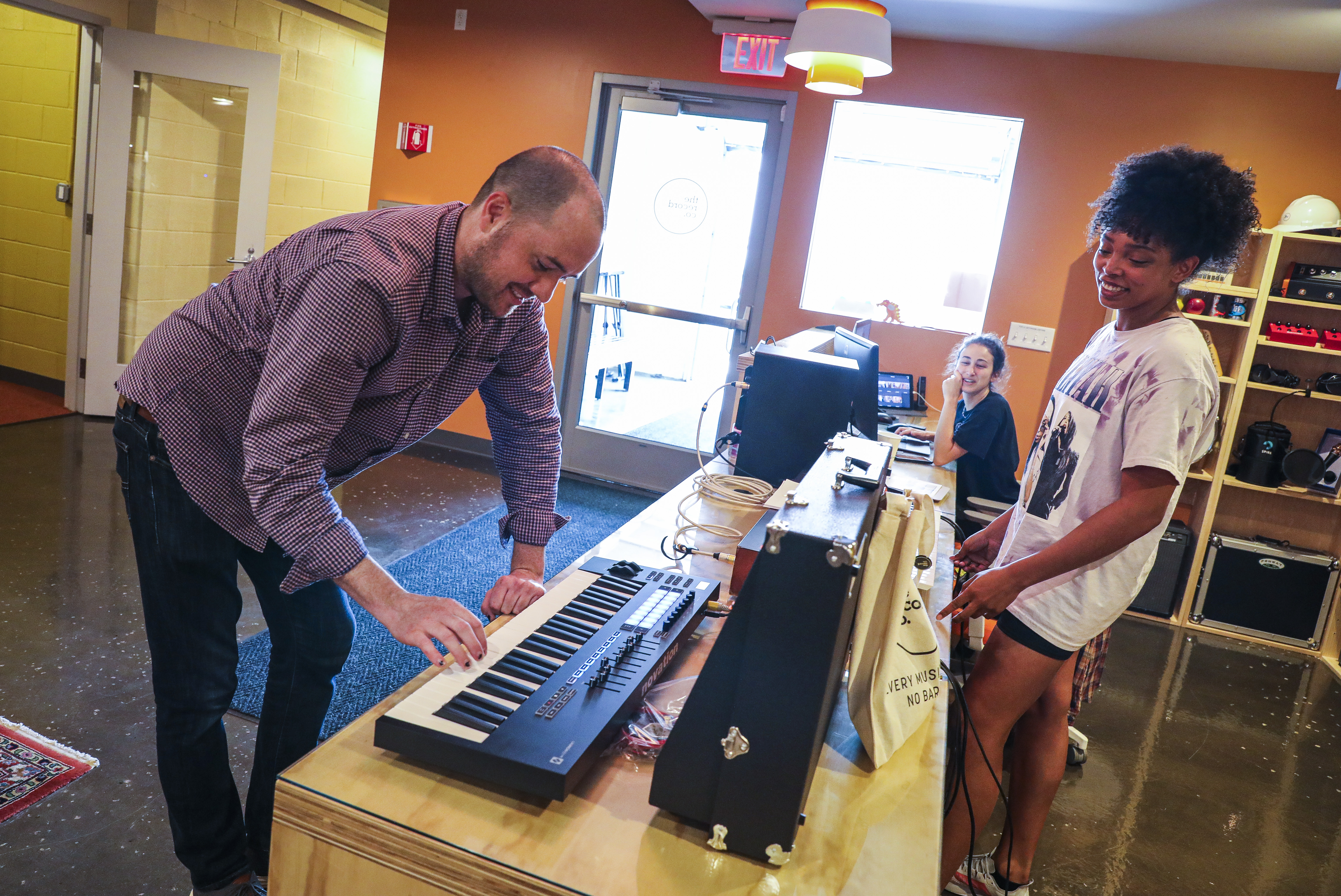 Founder and executive director Matt McArthur tries out a keyboard in the lobby of The Record Co. while Maria Bartolotta (center) and Ari O’Rourke look on.
