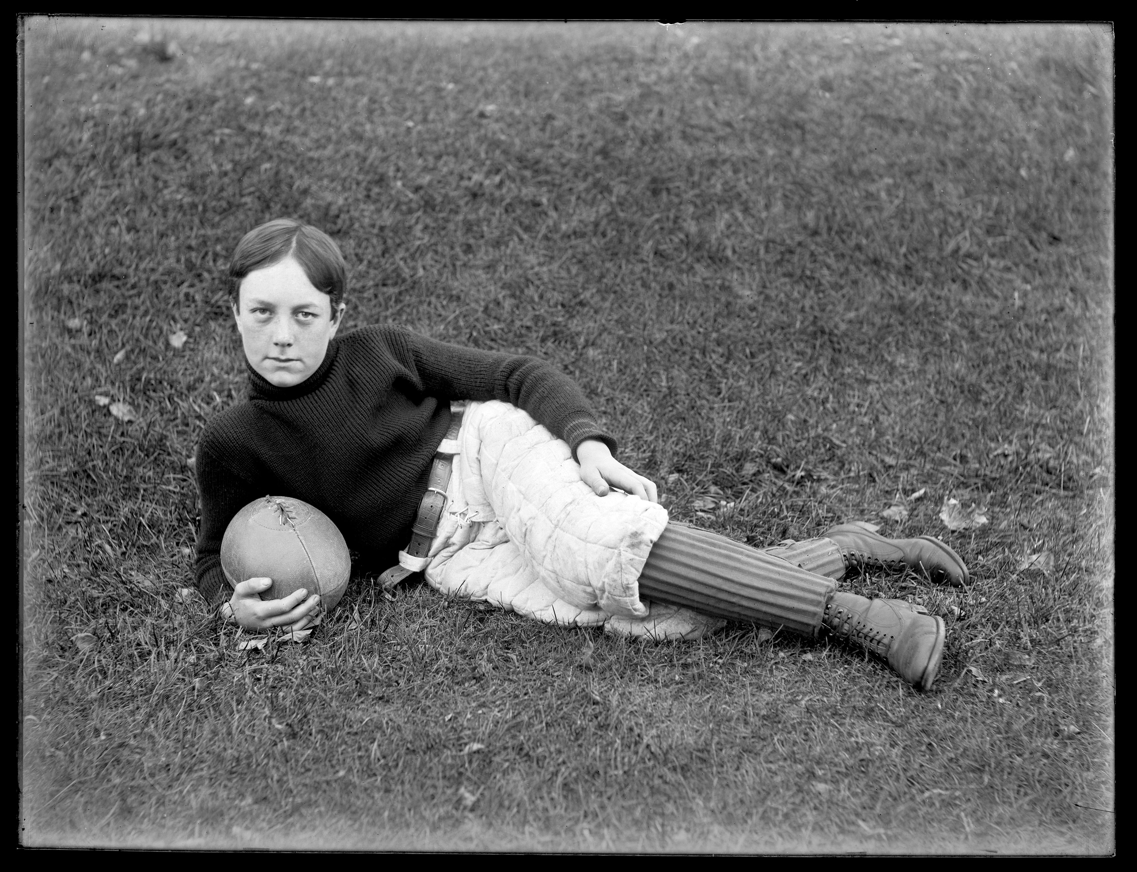 A young man with football clothing and ball. The image is from a glass plate negative and part of the "Somebody Photographed This" collection.
