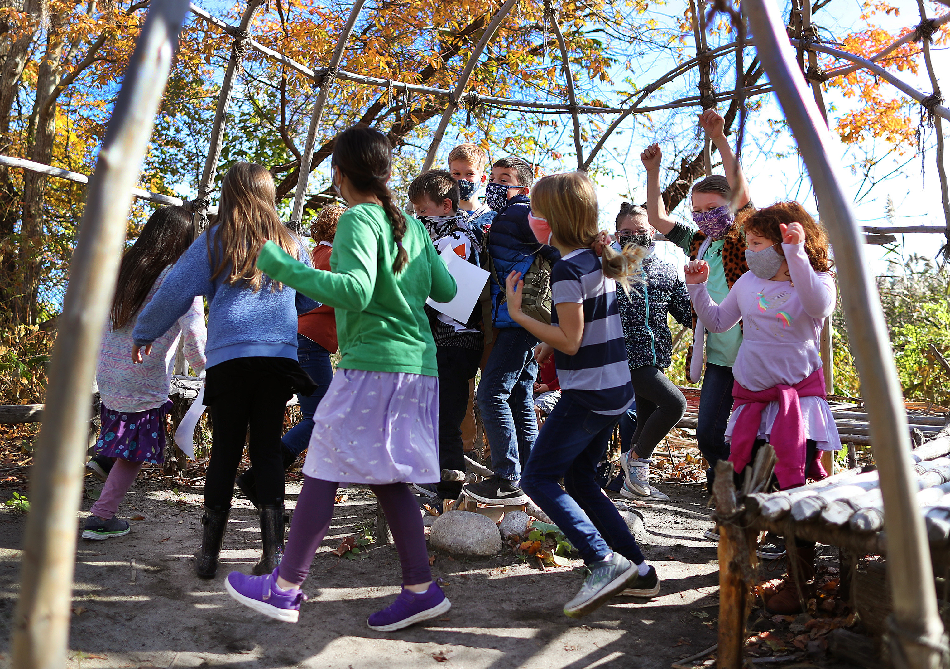 Youngsters walk in a circle inside the framework of the Summer House at the Wampanoag Homesite.