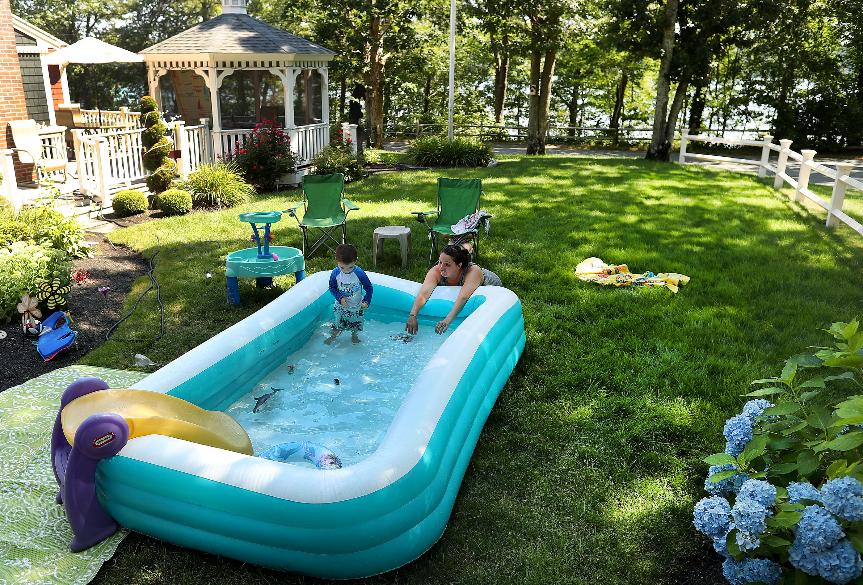 Tanya Mogardo played with her son, Landon, 2, in a swimming pool set up in the yard of her grandparents, Sandra and Bill Bolton, across the street from Shubael Pond.