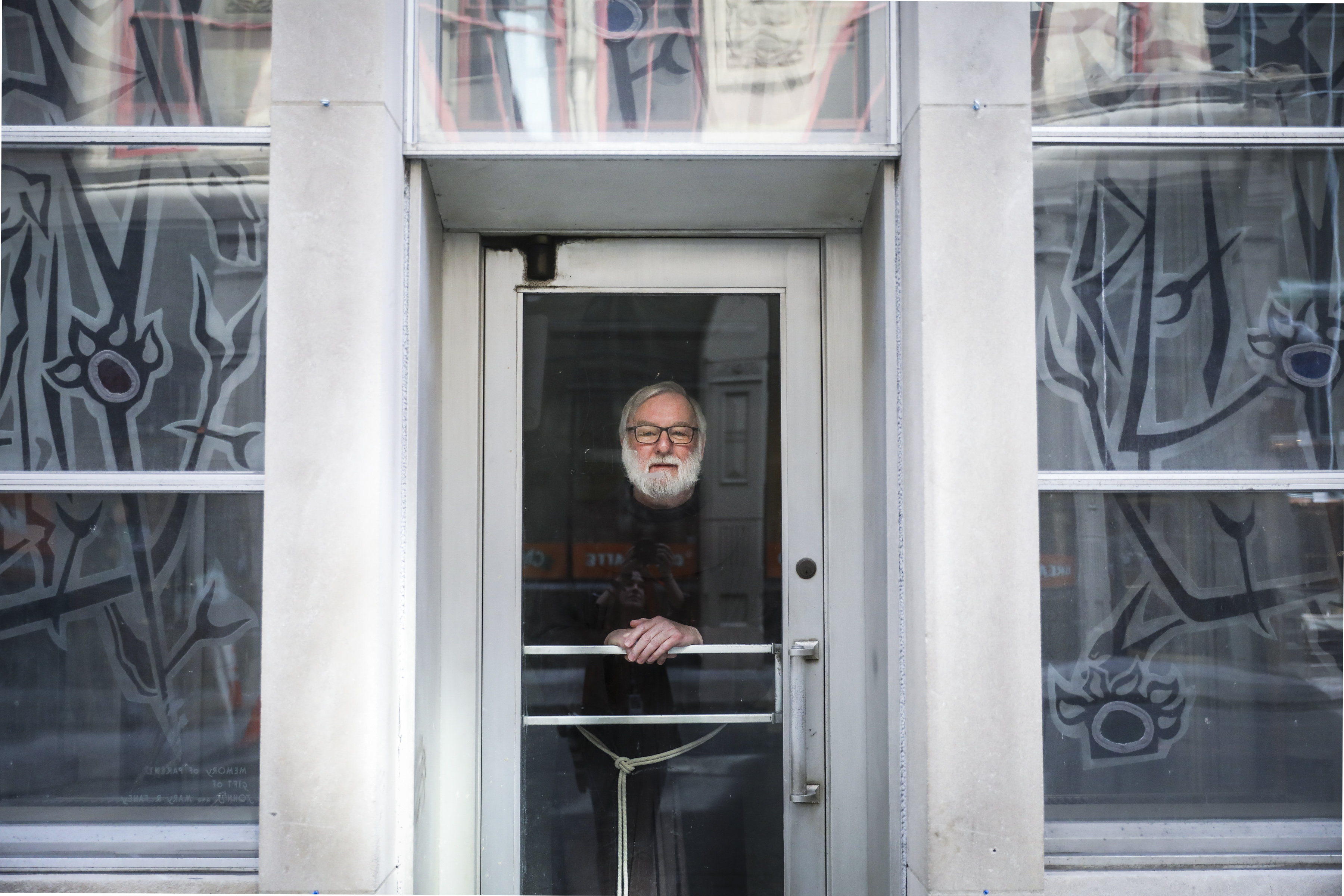 BOSTON  - 3/28/2020:  Father Richard Flaherty stands for a portrait while peering through the door of the St. Anthony Shrine in downtown Boston. (Erin Clark/Globe Staff)