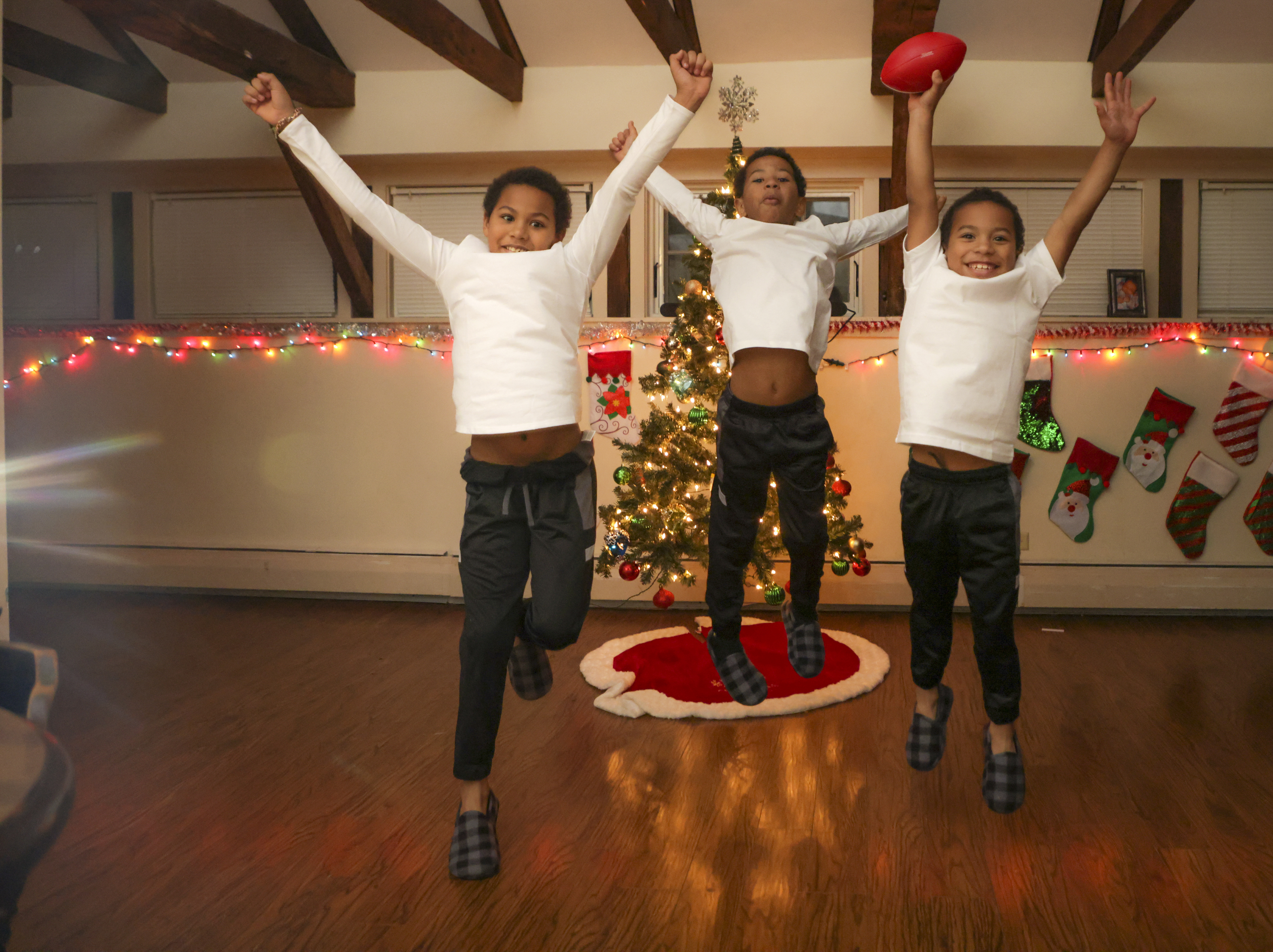 (Left to Right) Akai Fortes, 8, Isaiah Fortes, 10, and Rafael Ramos Alves, 6, all brothers, jumping in front of their Christmas tree in their living room.