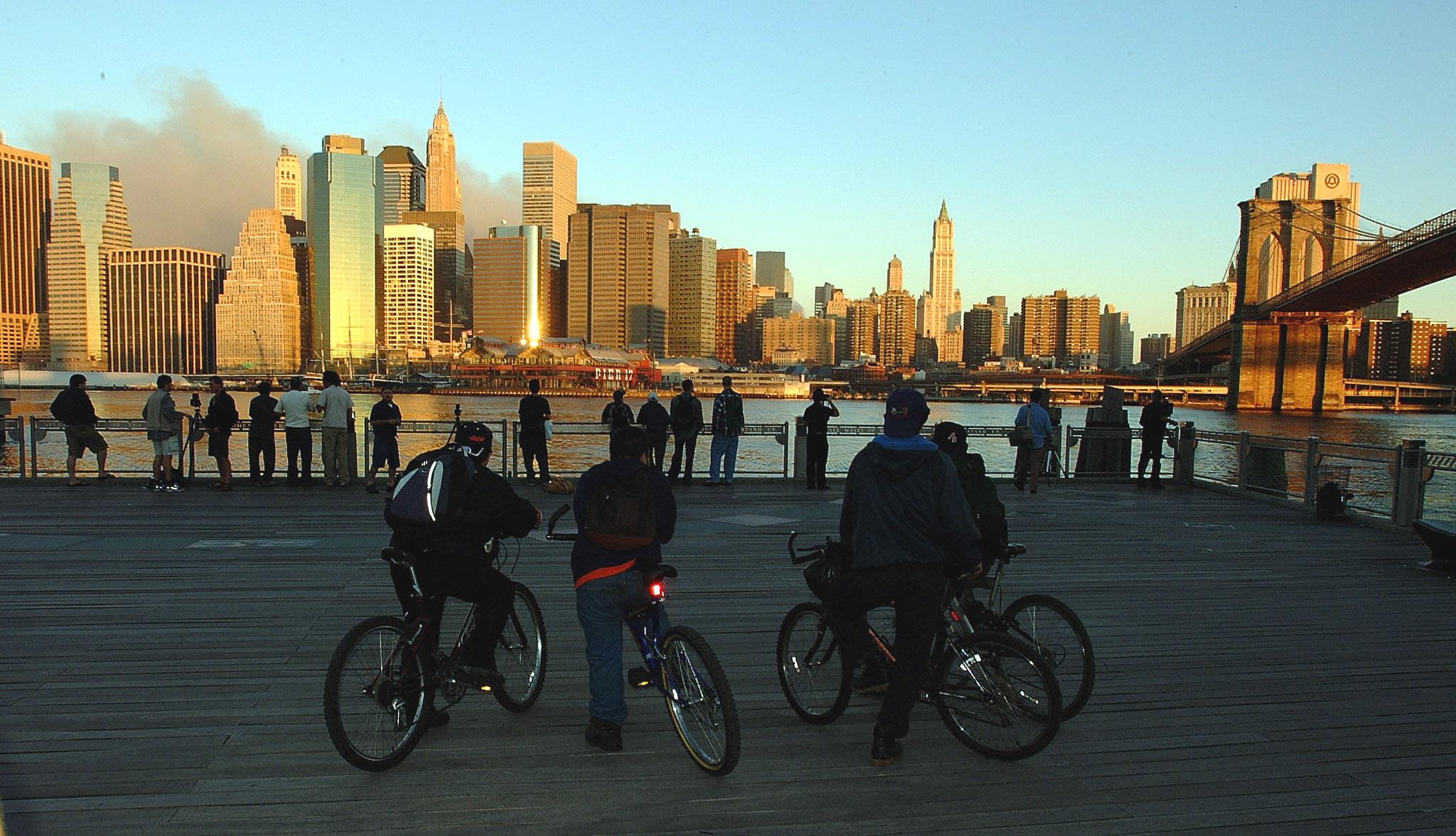 Smoke rises over the southern Manhattan skyline without the World Trade Center as members of the public watch from Brooklyn the following day.