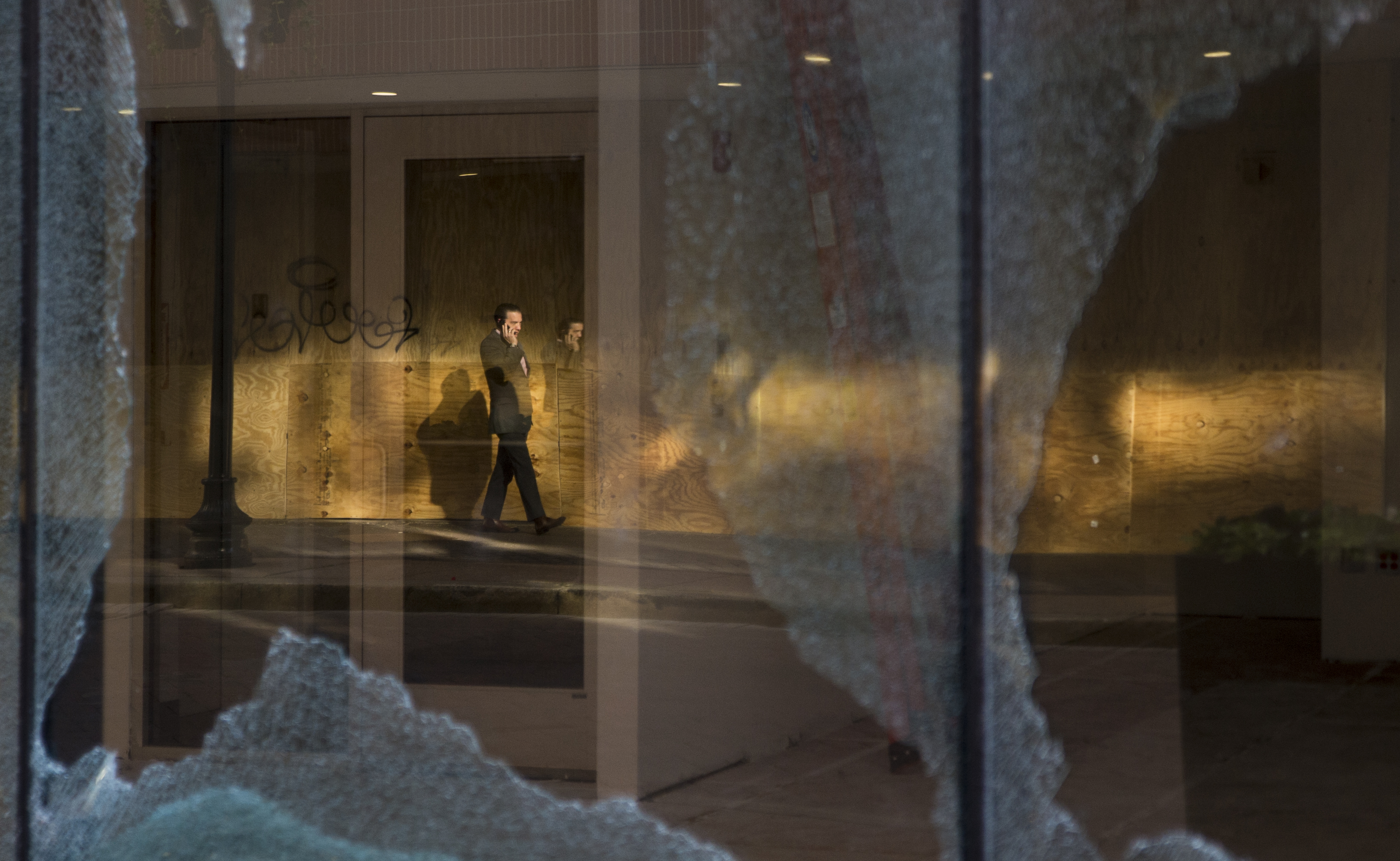 A man is reflected in the shattered storefront of retail space in Downtown Crossing on Monday.