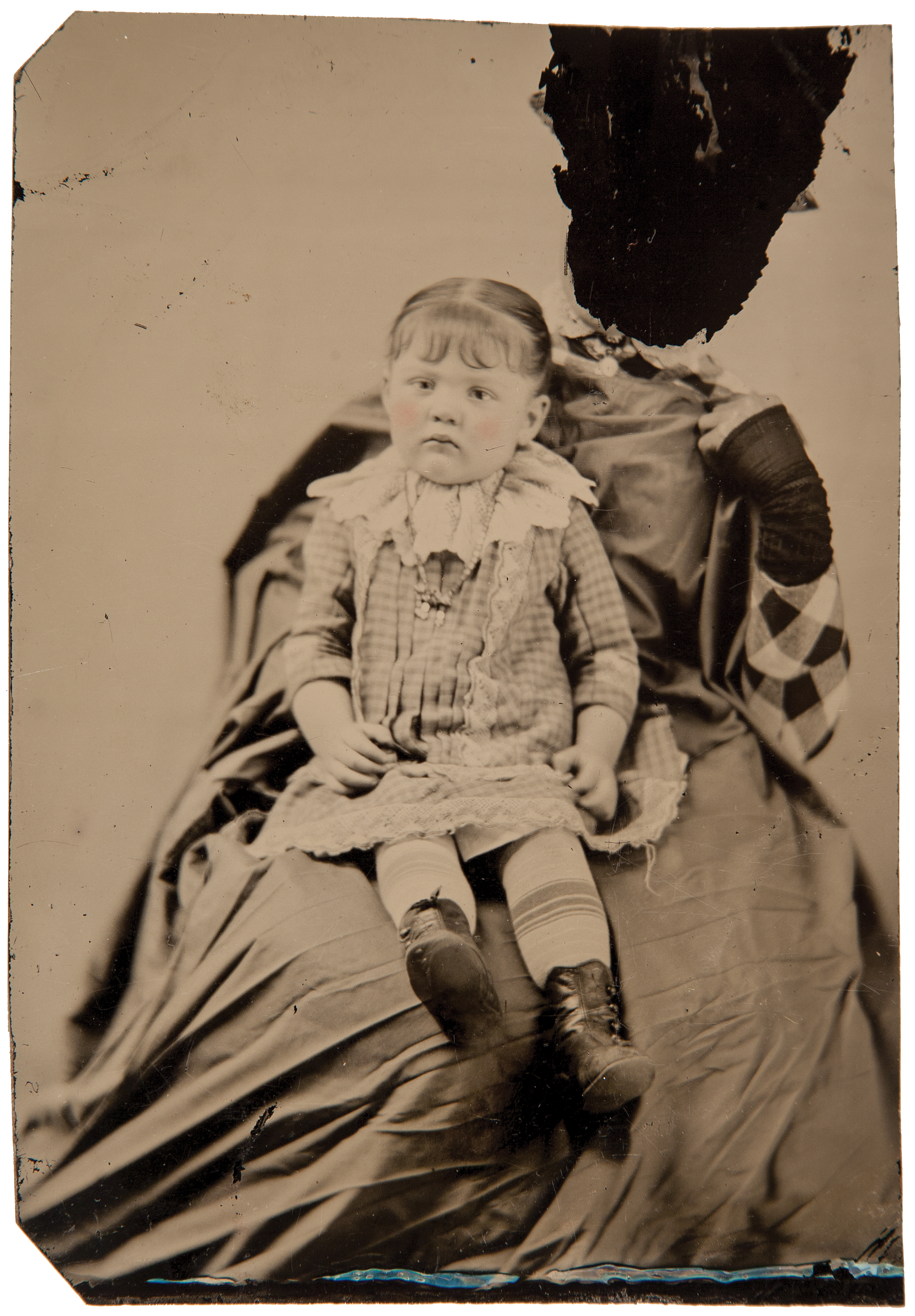 The face of this caregiver has been scratched away, exposing the black enamel tintype surface beneath it.