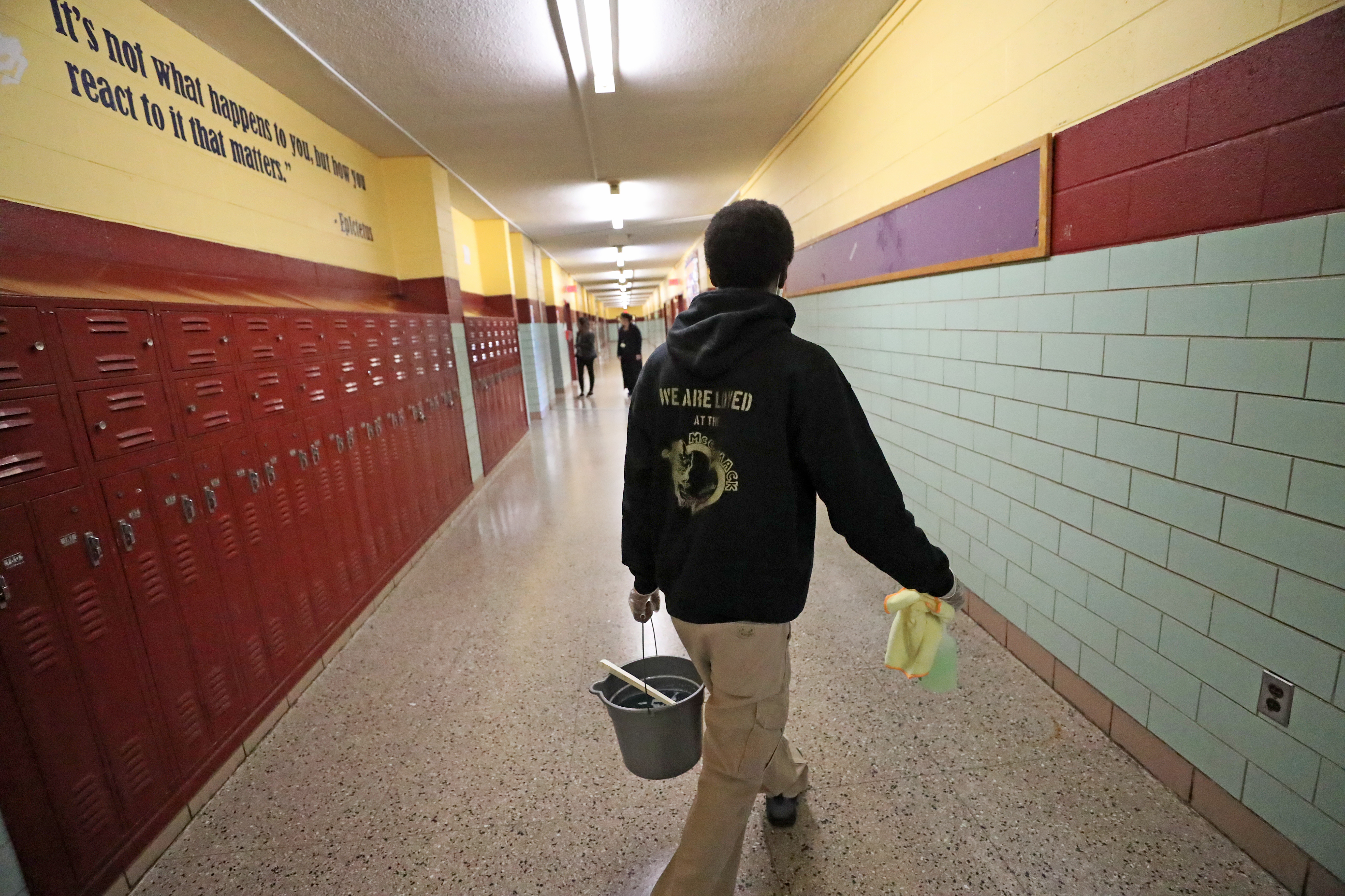 Earnest Bass, a custodian at McCormack Middle School in Dorchester, walked down the hallway with a bucket in hand as he finished cleaning a nurse's office restroom.