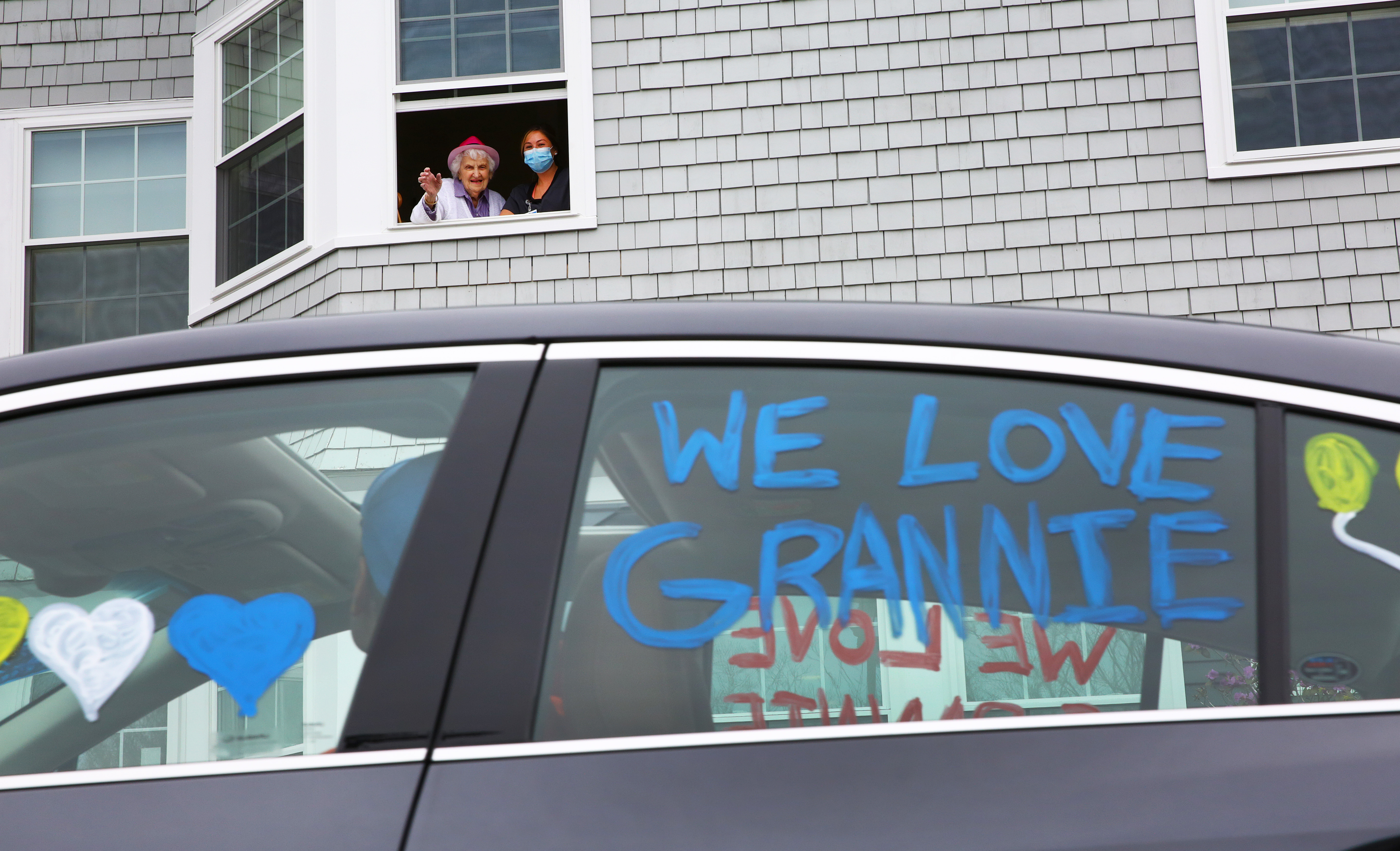 Peabody, MA  4/26/2020   Eleanor Dittmer, joined in the window by nurse's aide Courtney Nadeau, is a resident in the assisted-living unit of the Harriett and Ralph Kaplan Estates.  She is turning 93 on Wednesday, April 29.  Because of the COVID-19 pandemic, her family organized a drive-by birthday parade under her window.  Family (which included her children, grandchildren, great grandchildren, nieces, nephews, and others), friends and neighbors drove through the parking lot, escorted by police cars, a police motorcycle, tow trucks and a fire truck.  (Pat Greenhouse/Globe Staff)