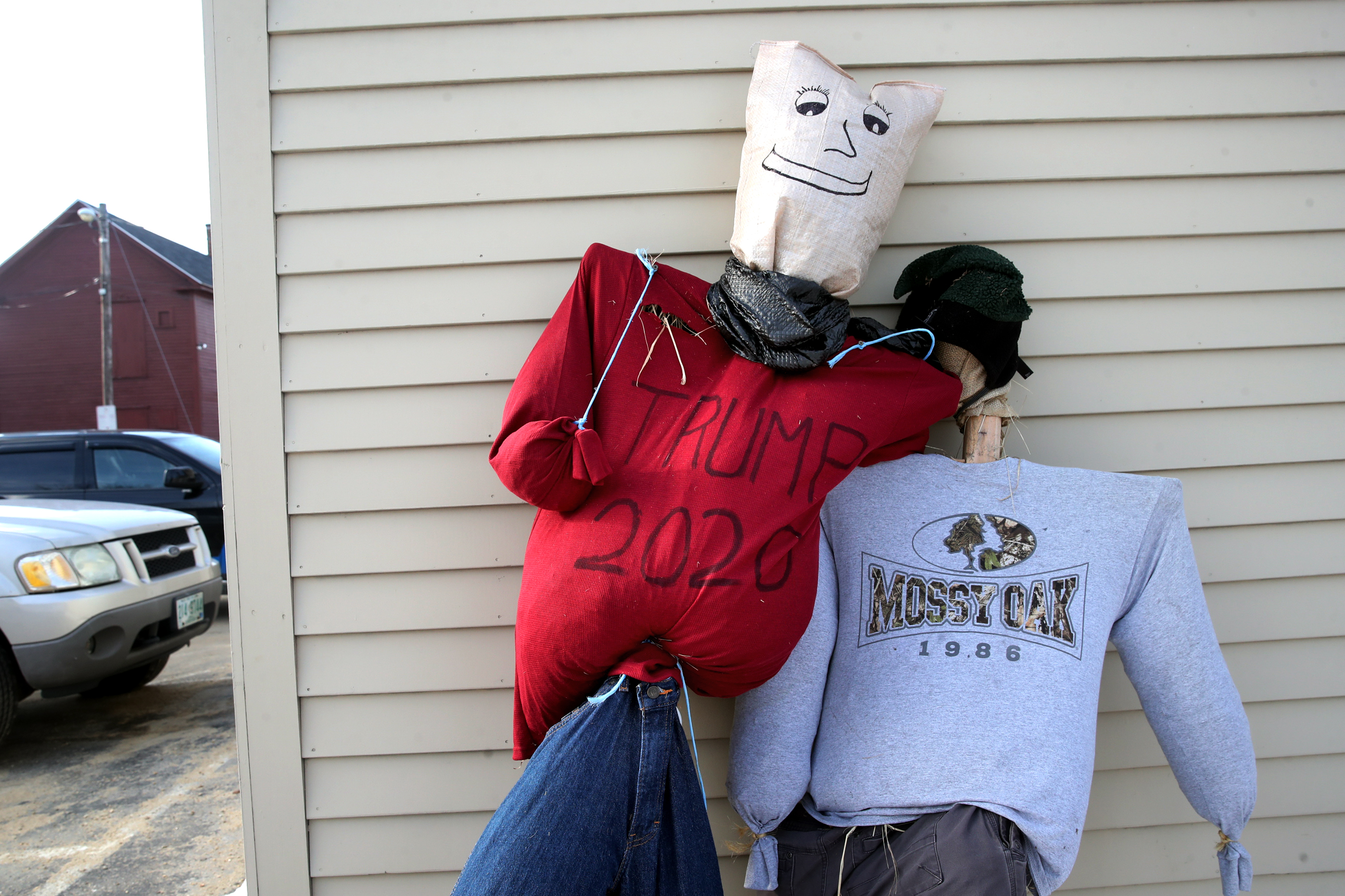 A pair of scarecrows, one with "TRUMP 2020" written on its shirt, rest against a wall at the police station in Troy, NH.