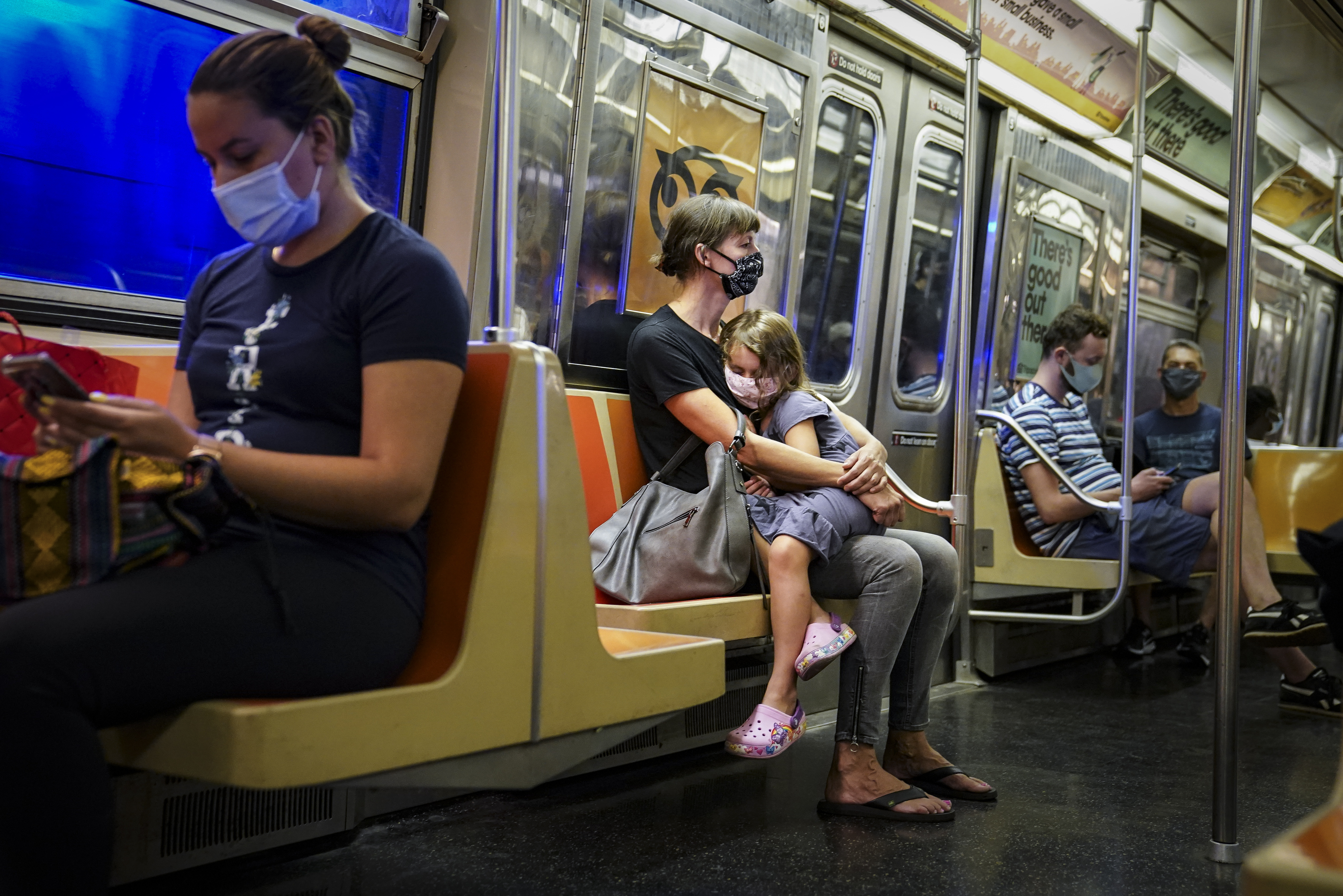 A child rested on a New York subway car while riders wore protective masks due to COVID-19 concerns.