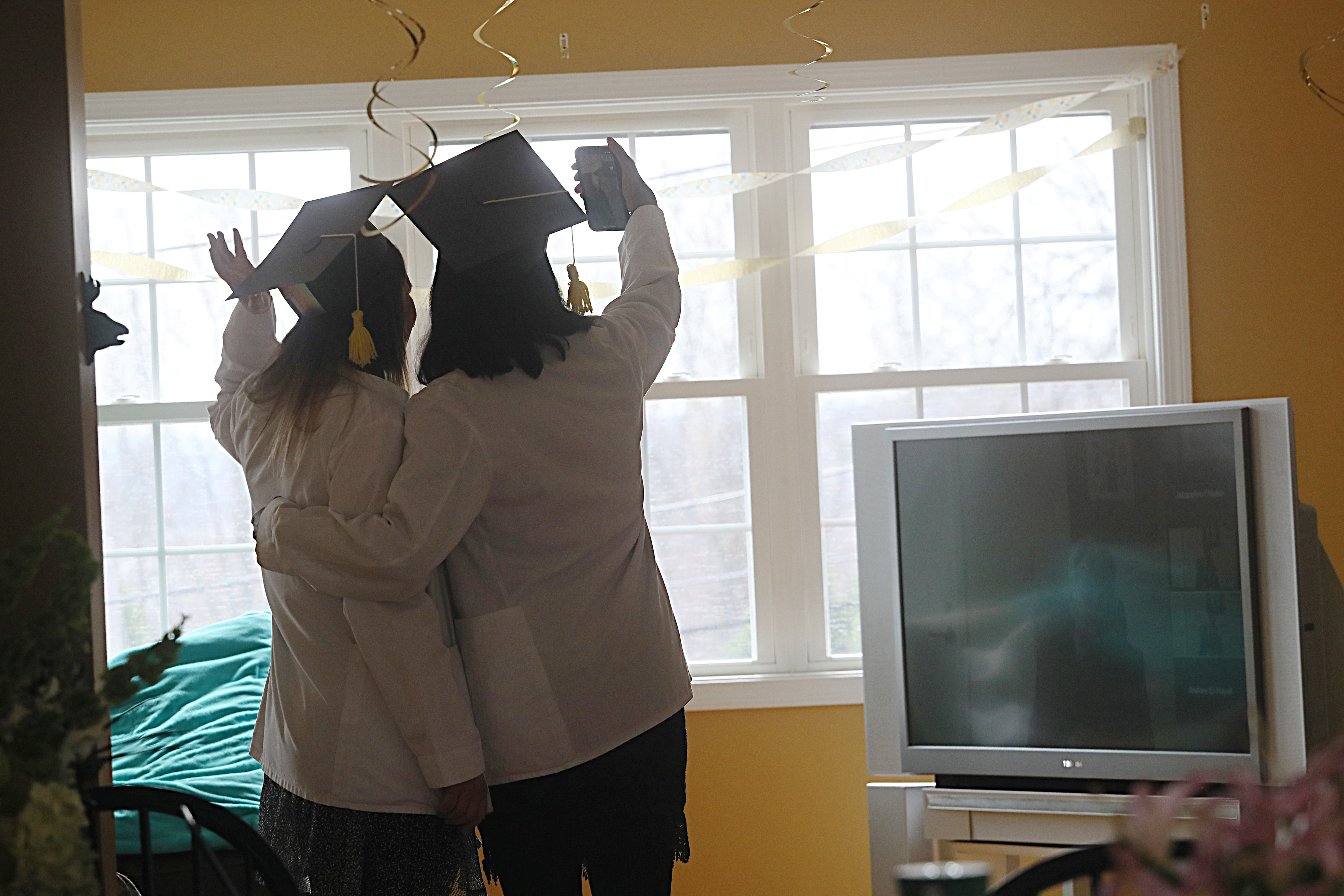 Worcester, MA 3/31/2020: University of Massachusetts Medical School graduates Shruthi Srinivas and Jacqueline Chipkin, right to left,  take a selfie during their two month early graduation which was  performed over Zoom via their TV   in their apartment due to coronavirus COVID-19. They wore their white coats because their gowns had not arrived yet, and their made their caps.  (Suzanne Kreiter/Globe Staff)