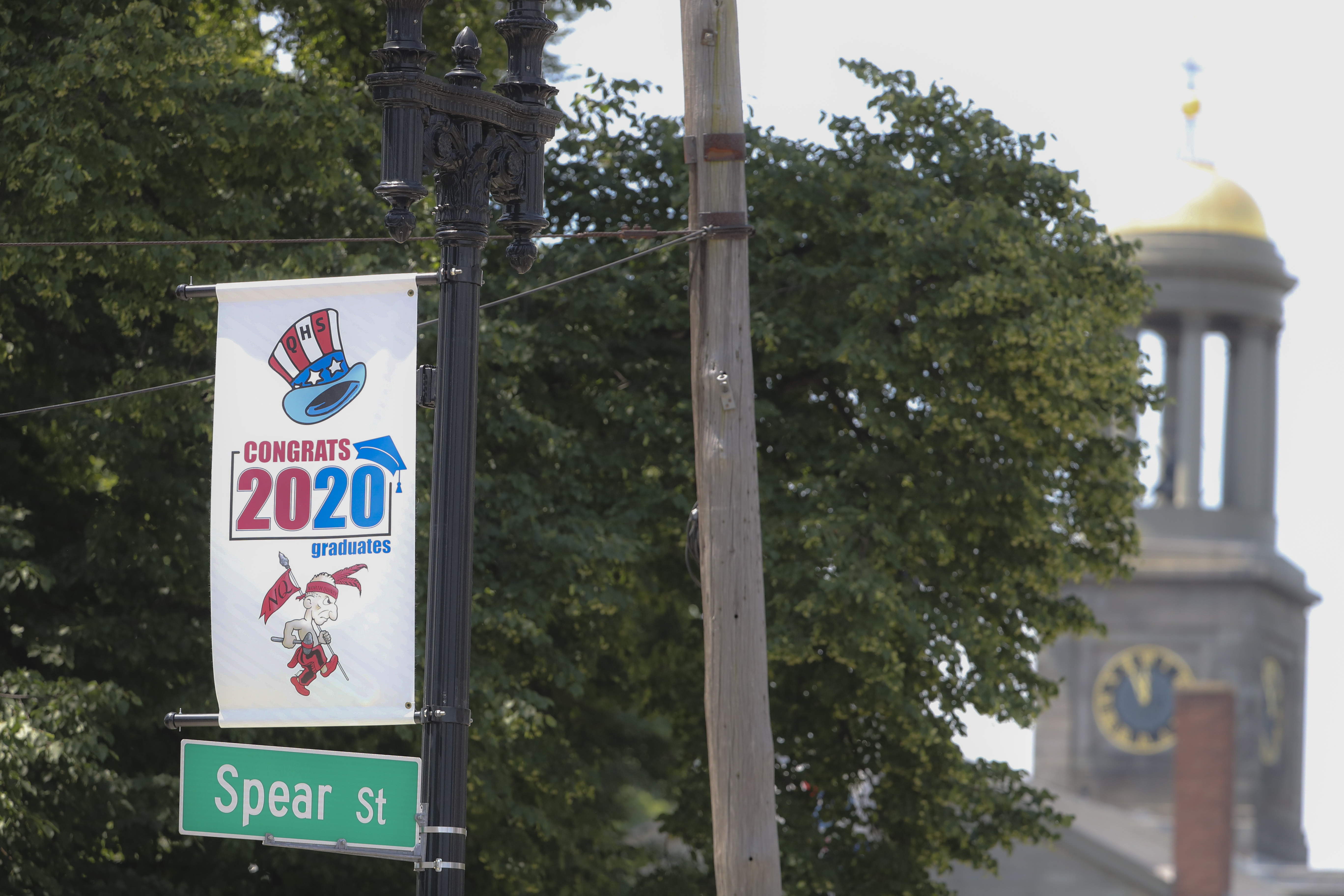 In Quincy Center, a banner congratulating the graduates of North Quincy High School depicts the mascot "Yakoo." In the background is the United First Parish Church.