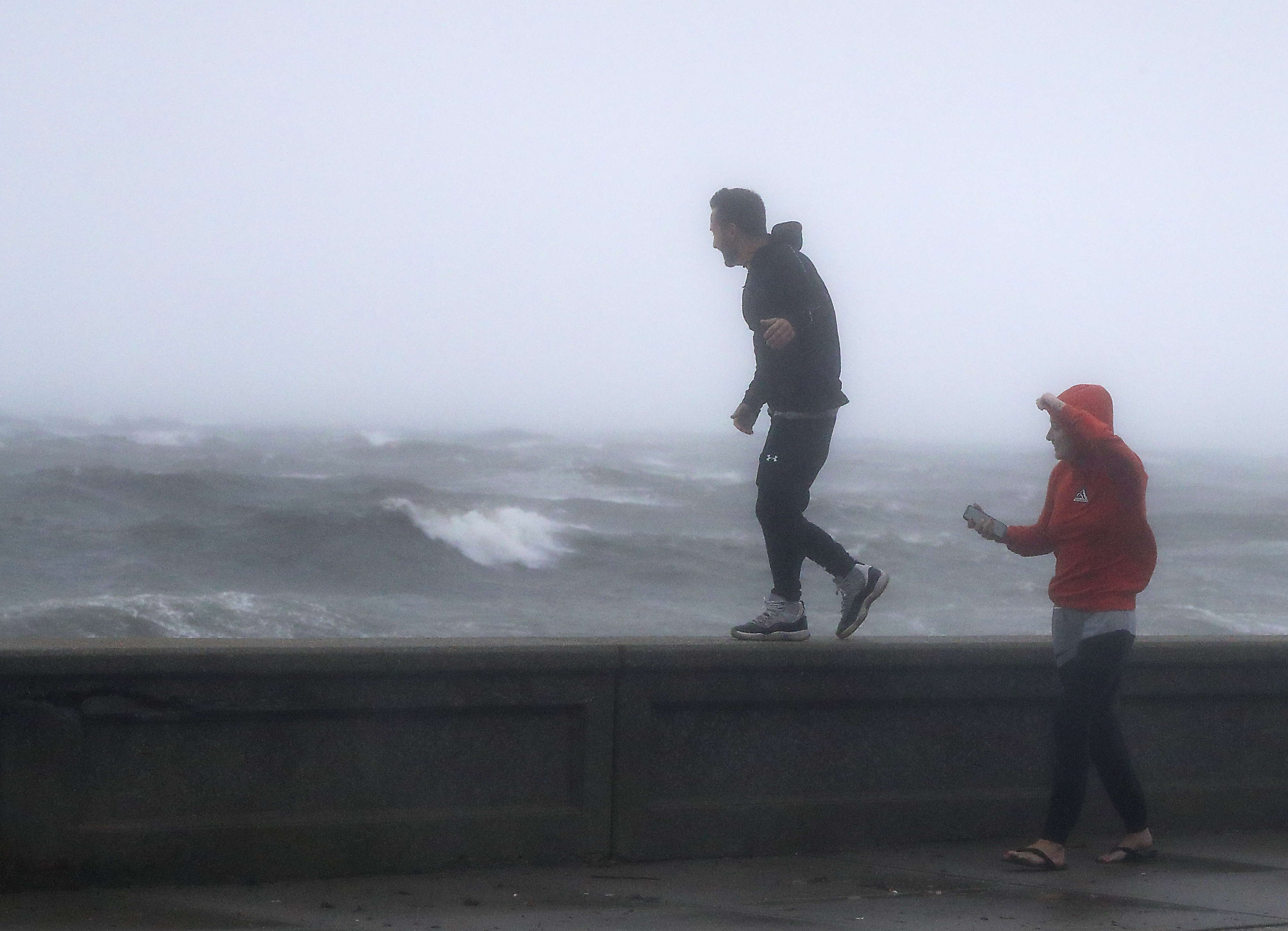 Matt Marsocci of Narragansett walked on the sea wall with wind gusts over 50 miles per hour, as his girlfriend, Morgan Demonti, watched during Tropical Storm Henri.