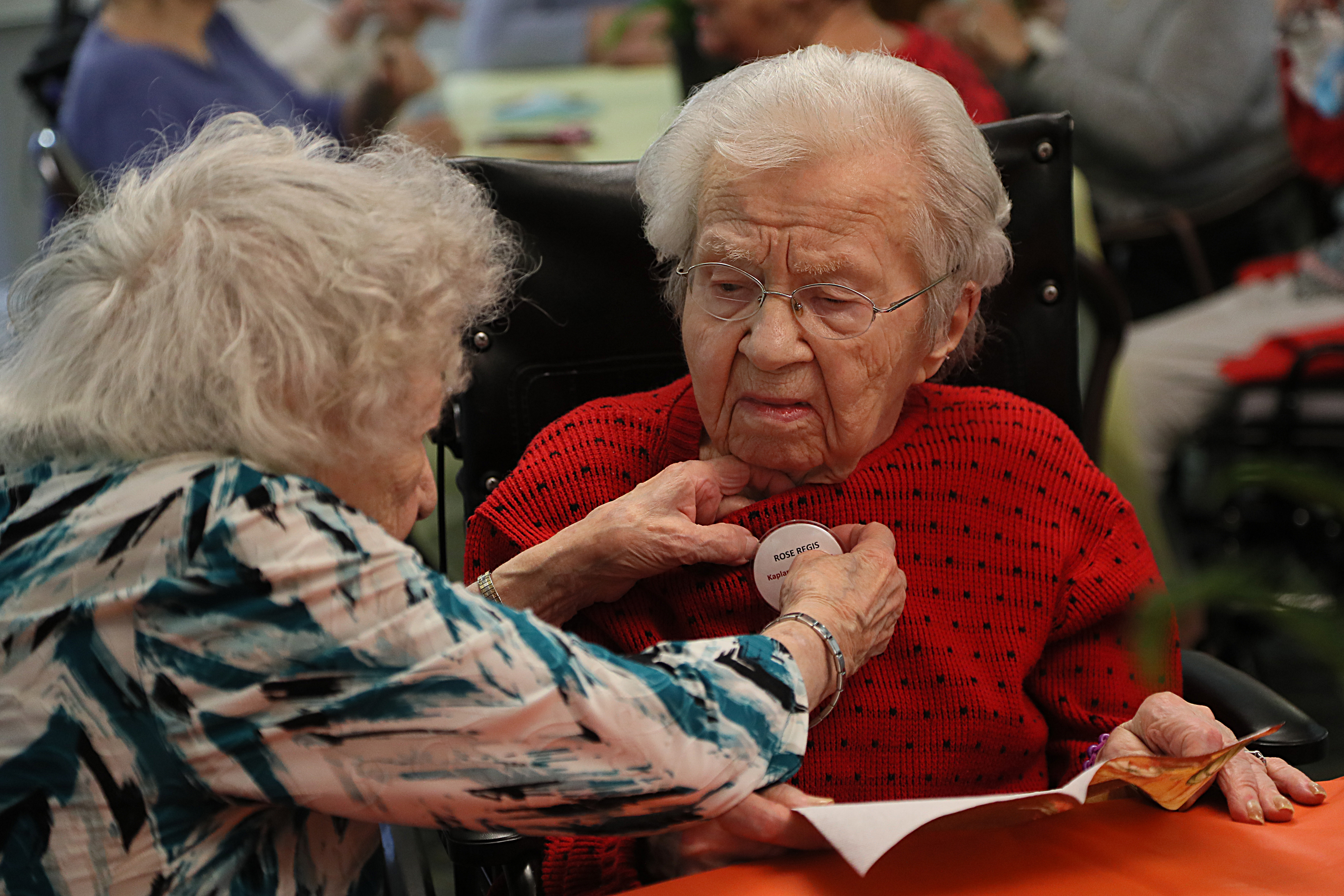 Kay Morrocco, 101, helps Rose Regis, 107, with her badge.  While there are differing opinions on why Century Club members live such long and independent lives, there is general agreement that they are proof that the aging process can be a process of aging. dignity, joy and humor.