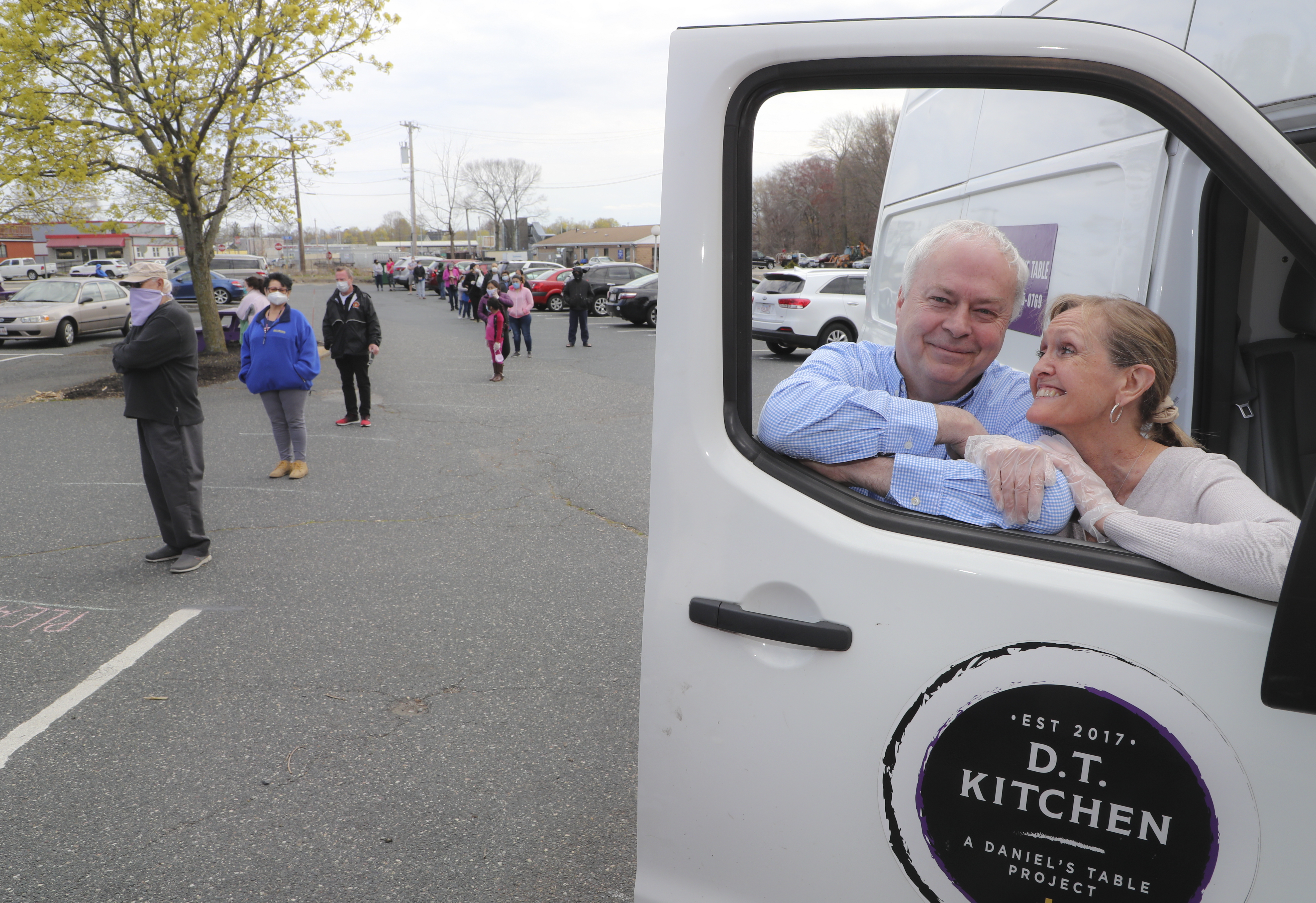Alicia and David Blais stand in the door of one of their delivery trucks while people wait in line for groceries. They founded Daniel’s Kitchen in November 2011 with the mission to feed families that need short-term help giving them a shopping bag with enough food for a family of four for one week. Since the coronavirus pandemic, they have seen a four-fold increase in needy families.