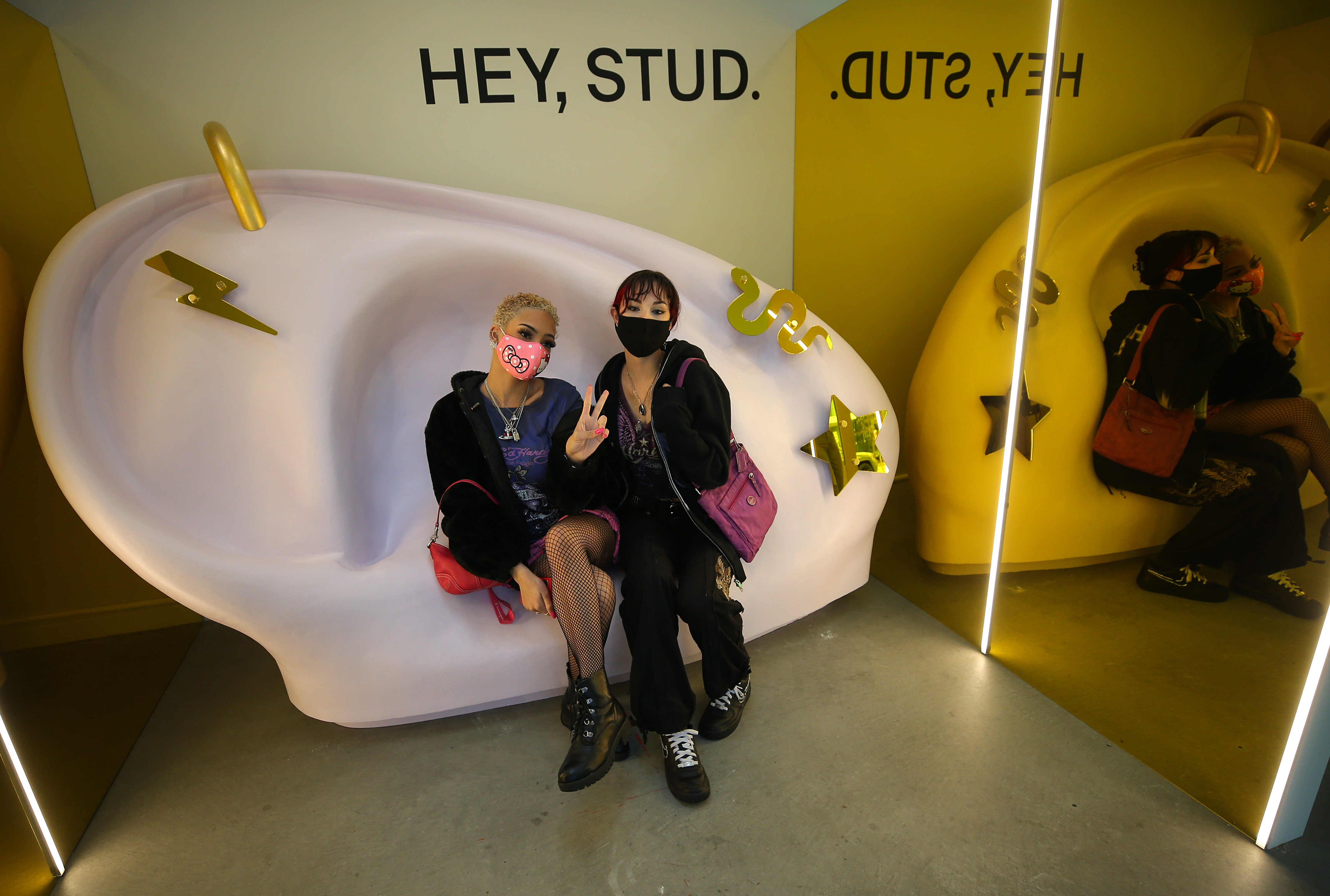 Samantha Jenkins and Sydney Pesaturo sit on a giant ear bench in the waiting room of Studs.