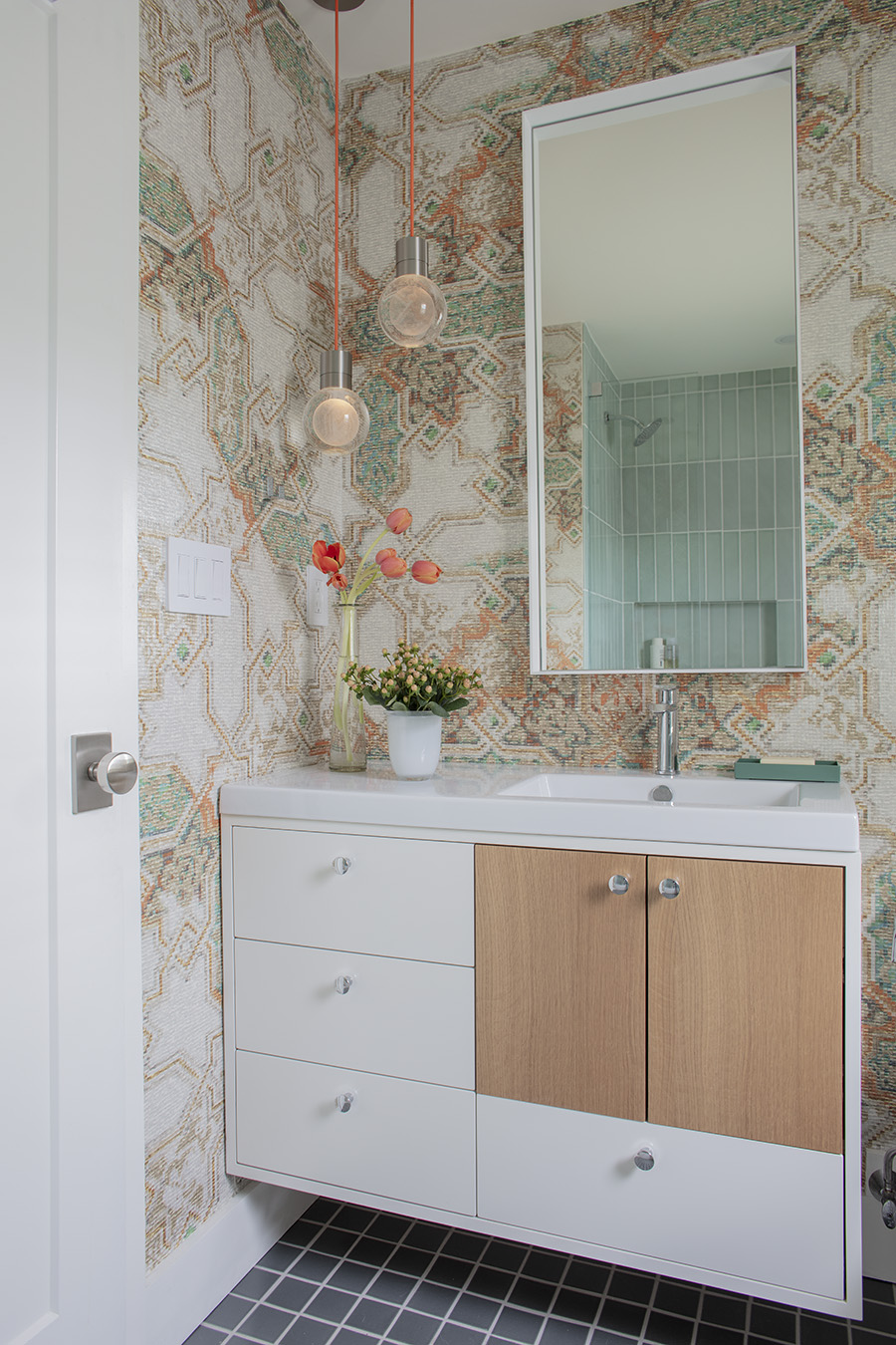 In the family bath, Hall made use of wall height gained from removing a soffit by hanging an extra tall mirror and a pair of floating orb pendants with orange cords.