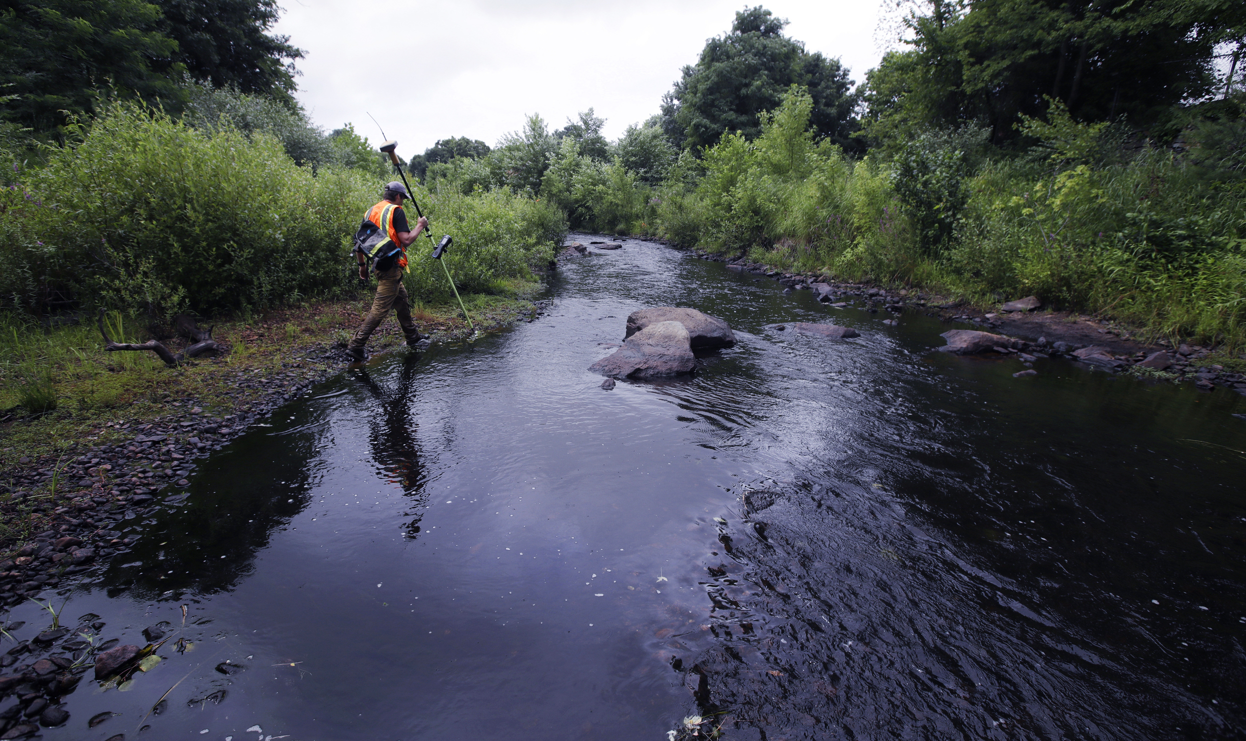 A surveyor walks the banks of the Mill River, at the site of the former Whittenton Pond Dam, just upstream from downtown Taunton, Mass., July 25, 2018.