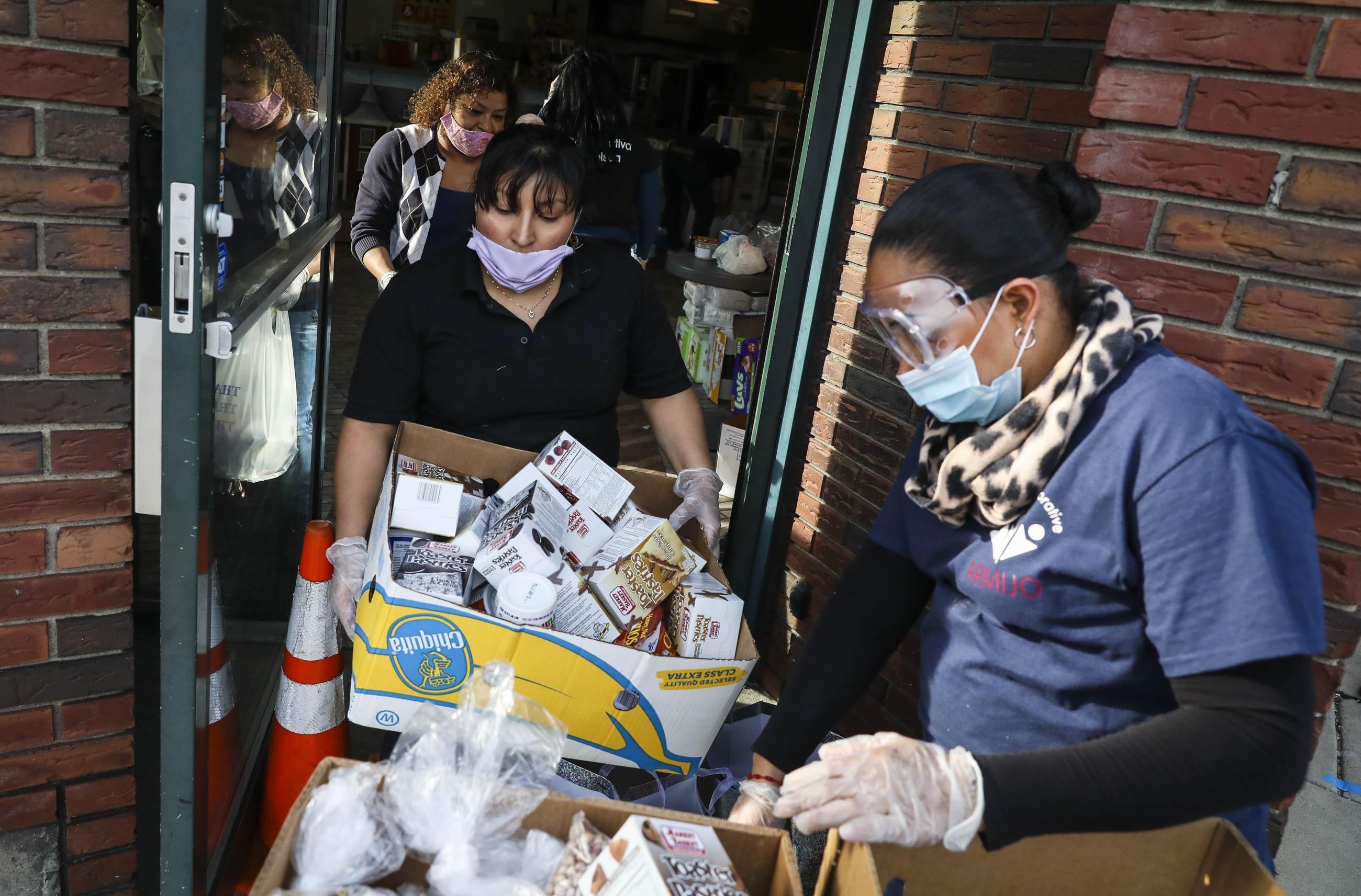 CHELSEA - 4/14/2020:  Gladys Socop, left, brings out a box of groceries to Jessica Armijo, right,  while volunteering in a pop-up food pantry hosted by Pan Y Cafe. Organized by Chelsea Collaborative, the food distribution has been operating for over 3 weeks with food donated by local businesses and food pantries and delivered to at-need families in Chelsea.  (Erin Clark/Globe Staff)