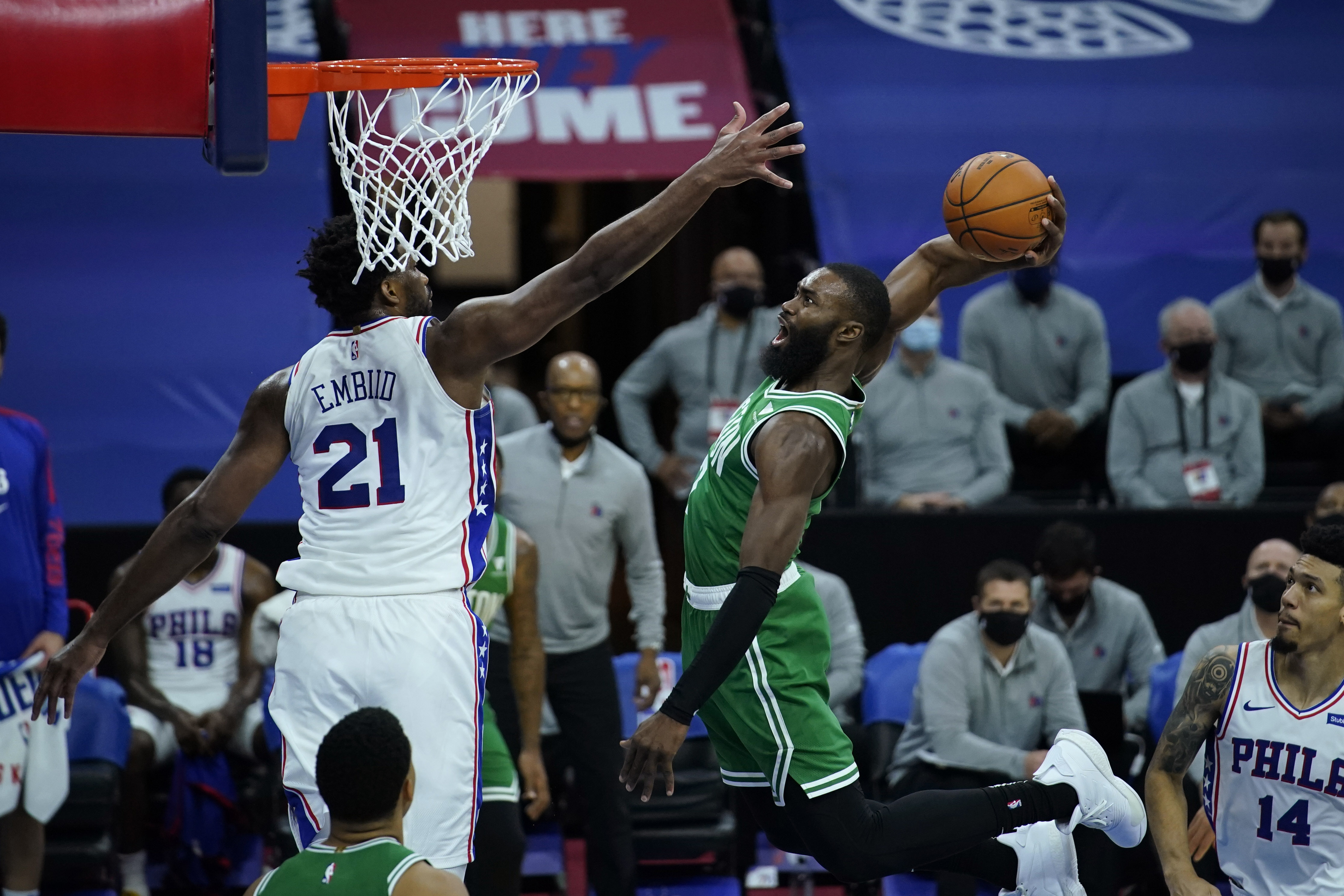 Jaylen Brown soars in for a dunk despite the defense of the 76ers' Joel Embiid.