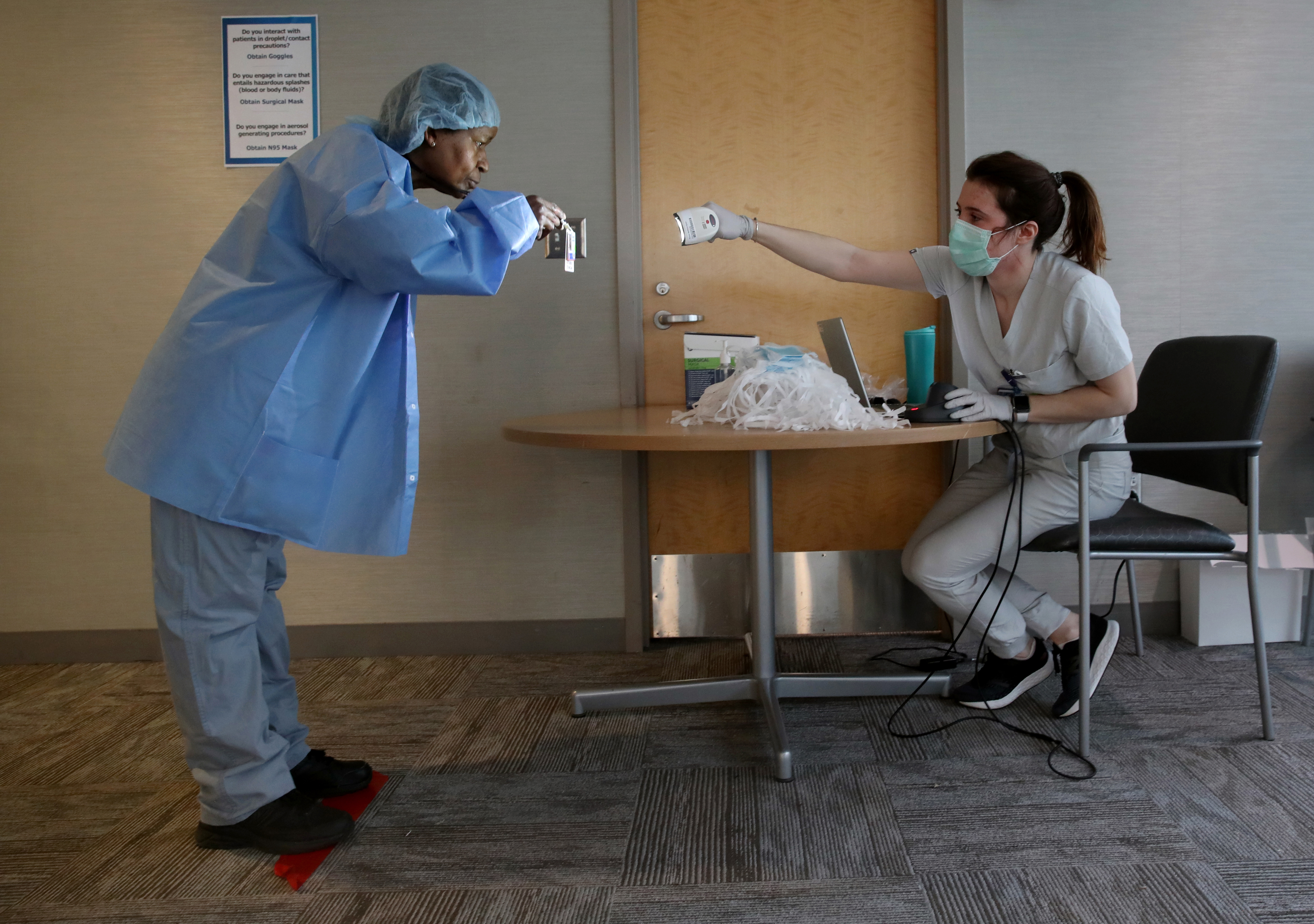 Boston,MA - 3/25/2020: Medical assistant Eileen Monagle, right, scans a staff members identification badge in a personal protective equipment distribution area at Brigham and Women's Hospital in Boston, MA on March 25, 2020. The badges are scanned to keep track of PPE inventory. Monagle was distributing personal protective equipment to staff including face shields, eyewear, and procedure and surgical masks. (Craig F. Walker/Globe Staff)