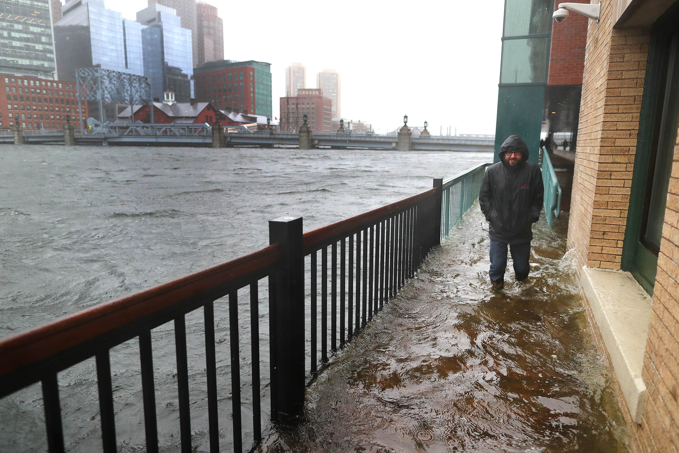 A man walks slowly through a flooded sidewalk off Congress Street during a storm, where water was flowing over from Fort Point Channel in the Seaport district in 2018.