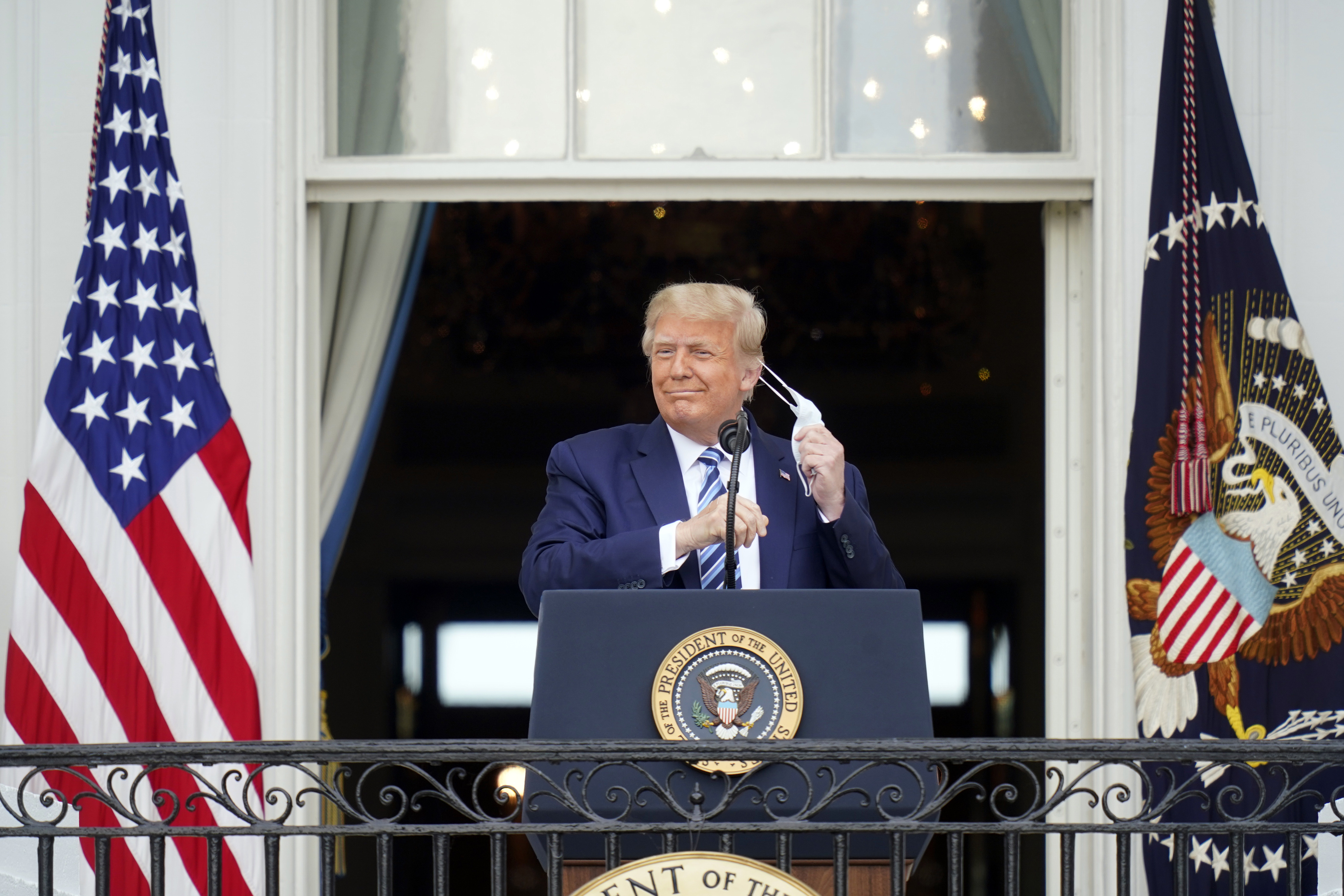 President Trump takes off his face mask as he appears on the balcony during a rally at the White House in Washington on Saturday, Oct. 10, 2020, his first public event since being hospitalized for COVID-19.