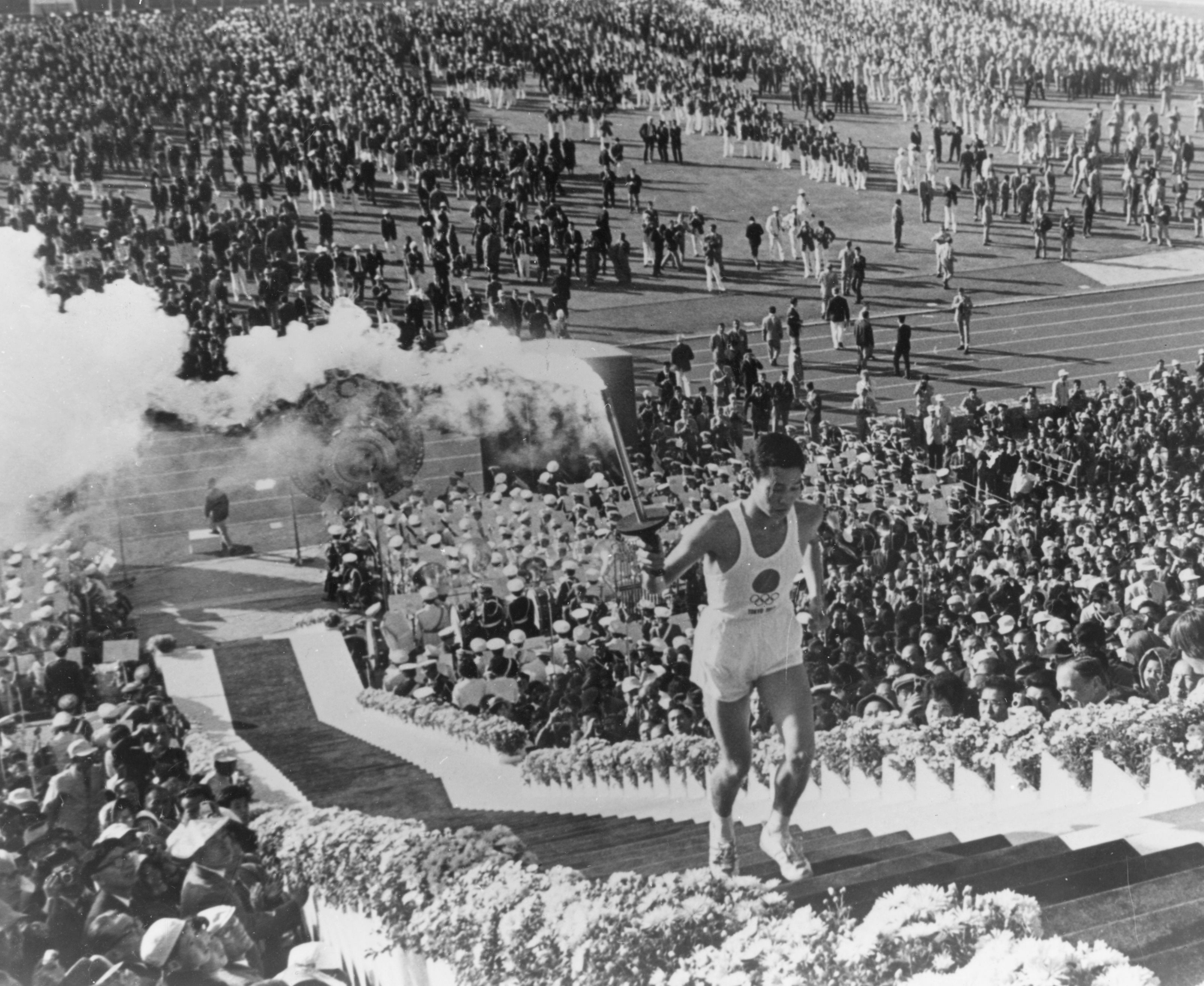 Yoshinori Sakai, who was born in Hiroshima on the day the first atomic bomb was dropped, carries the torch up to light the cauldron and start the 1964 Olympic Games.