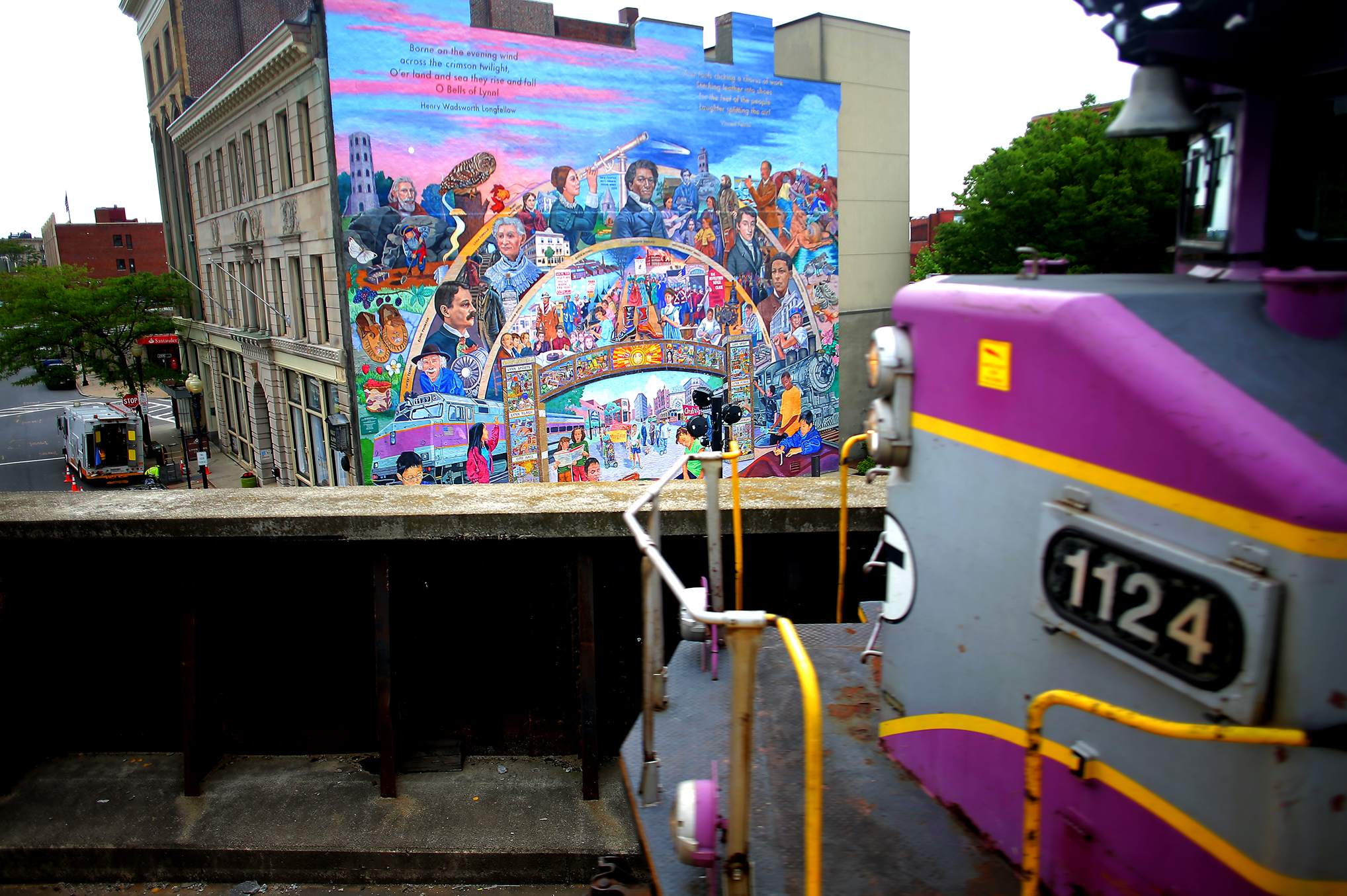 An MBTA commuter rail train pulled out of Lynn station in front of the mural “The Stories of Lynn” by David Fichter, Yetti Frenkel, and Joshua Winer.