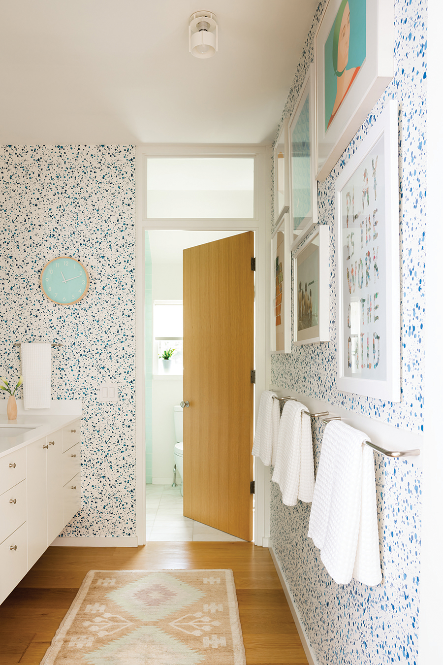 A transom window above the door to the shower and toilet lets light into the washroom area. The wallpaper is by Hinson.