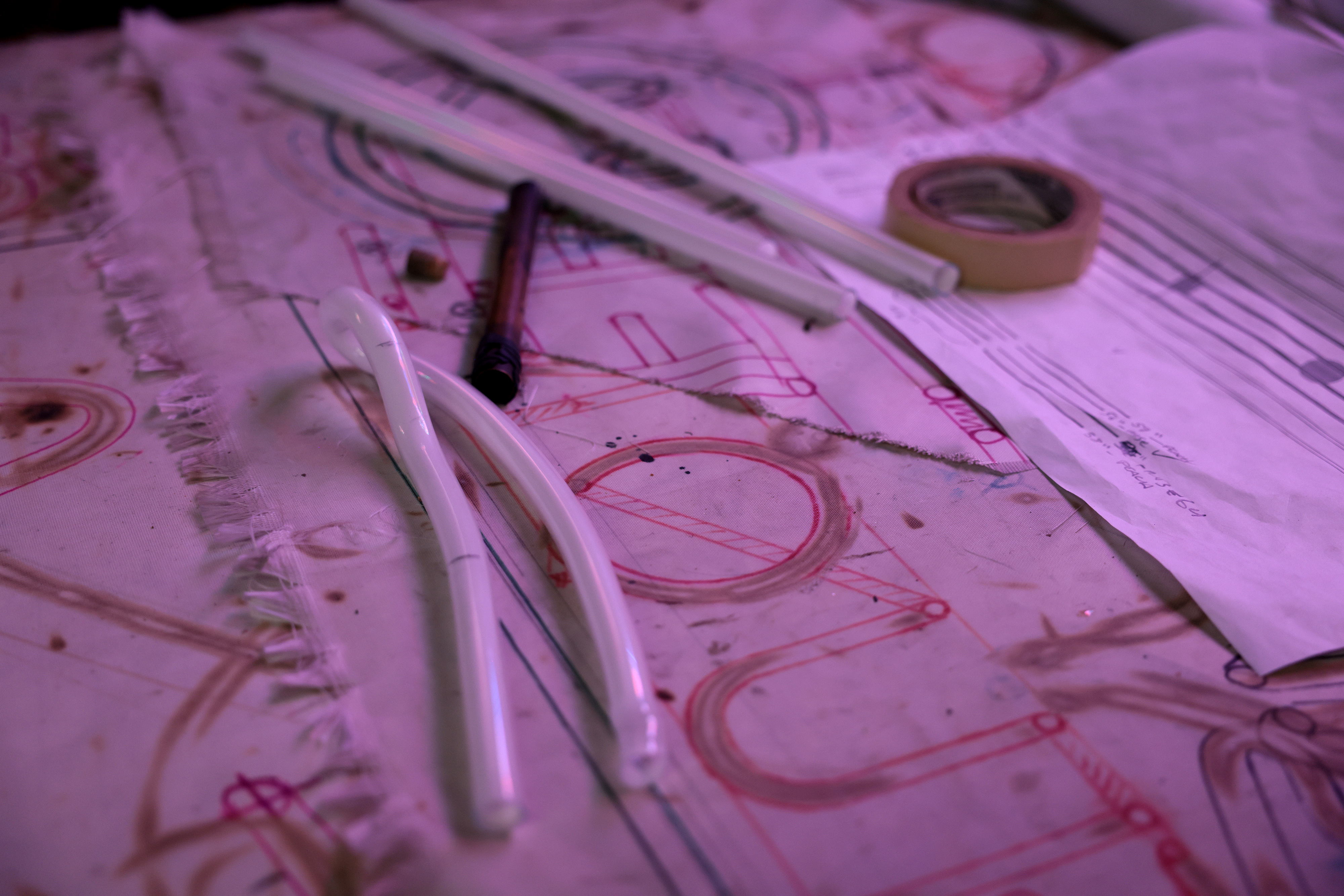 Pieces of glass tubing are seen against a table with sketches of the neon sign, which serve as a pattern for the bending process at Neon Williams in Somerville.
