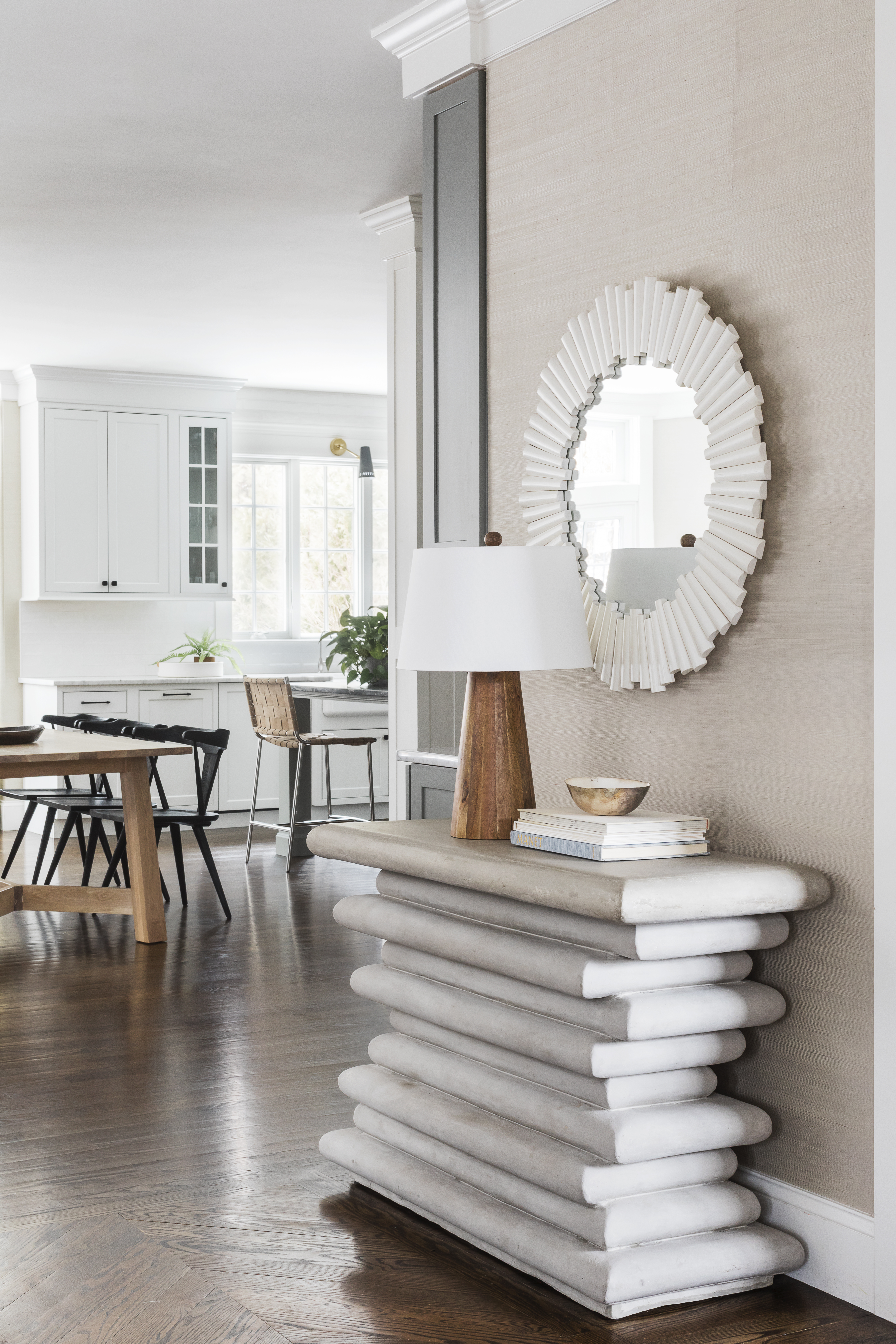 The entry vignette includes a Made Goods stacked concrete console and a Selamat painted rattan mirror. Grass-cloth wallcovering warms the space and ties it to the great room. Repetition of textures and neutral tones provide calmness and continuity.