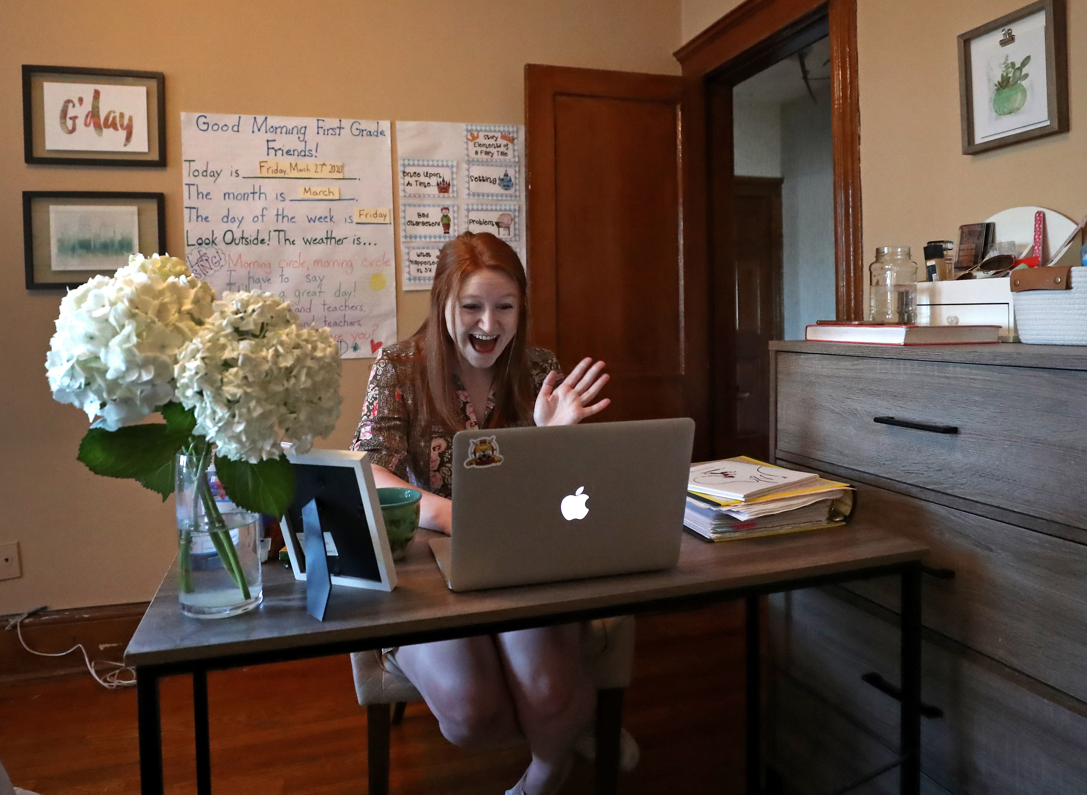 BROOKLINE, MA - 3/27/2020: Ellie Lyons waves good morning to students. She has converted the backdrop of the bedroom in her Brookline apartment into a makeshift first-grade classroom to make her students more comfortable. She meets with her Natick first-graders on Google Meet. Suburban schools are converting to online education as rapidly as possible, as some parents demand more formalized schooling amid the shutdown. (David L Ryan/Globe Staff )