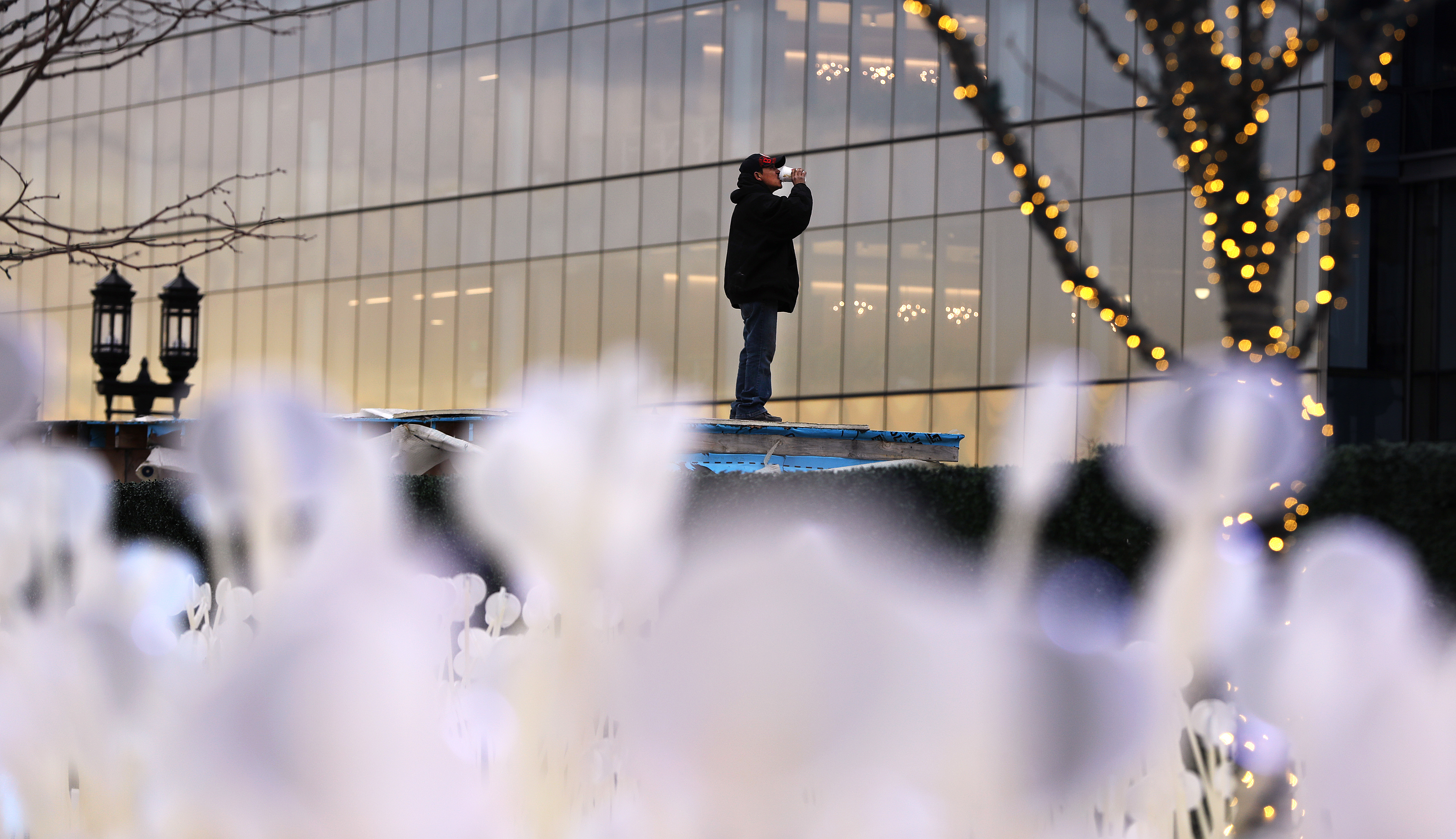 Framed by the tops of the nearby “Entre les rangs” art installation in the Seaport District, Noel Moncada took a quick sip between making repairs to a roof on January 6.