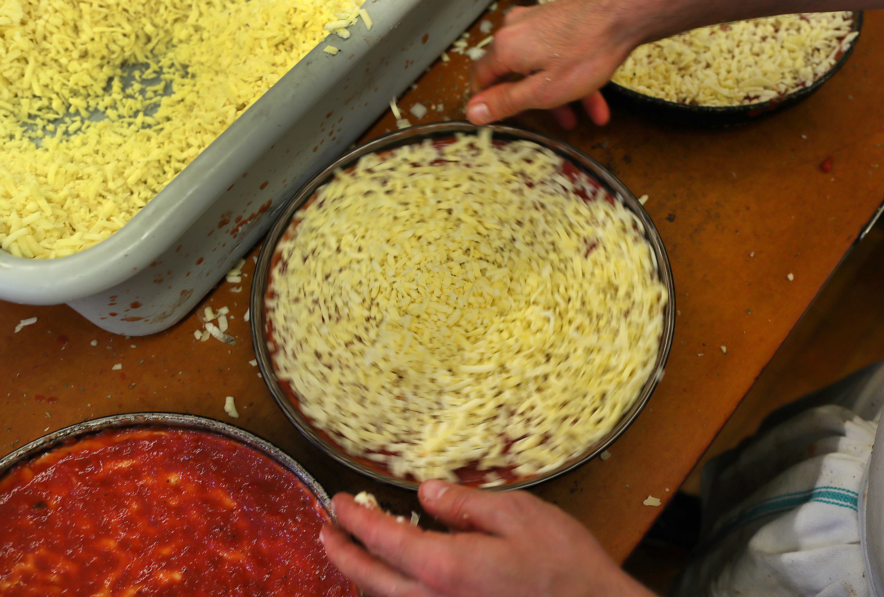 A pizza pan is twirled as it gets the cheeses put on top at the Lynwood Cafe.