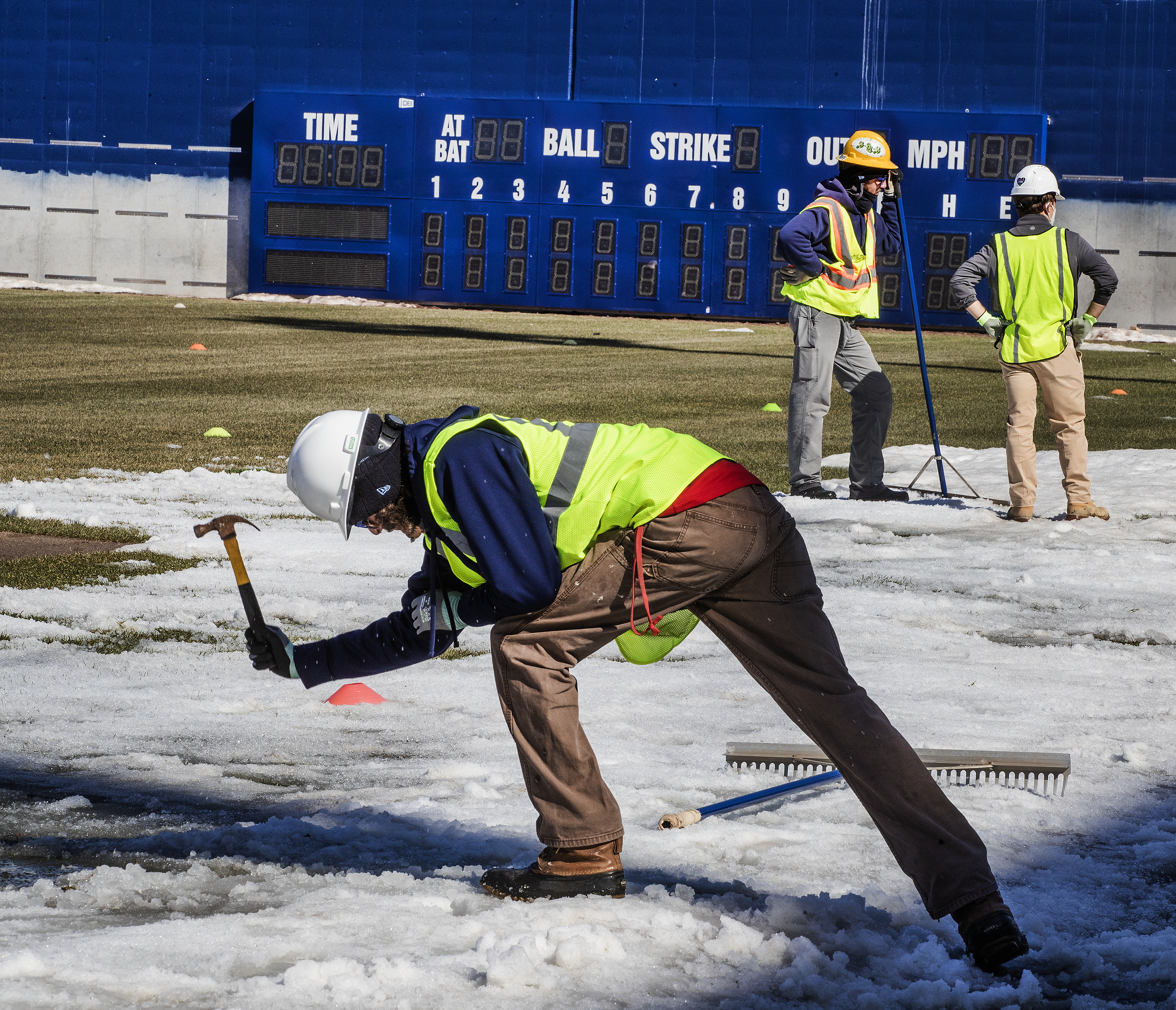 A worker used a hammer to break up the ice at Polar Park. Behind him is the 22-foot high blue wall in the right field.